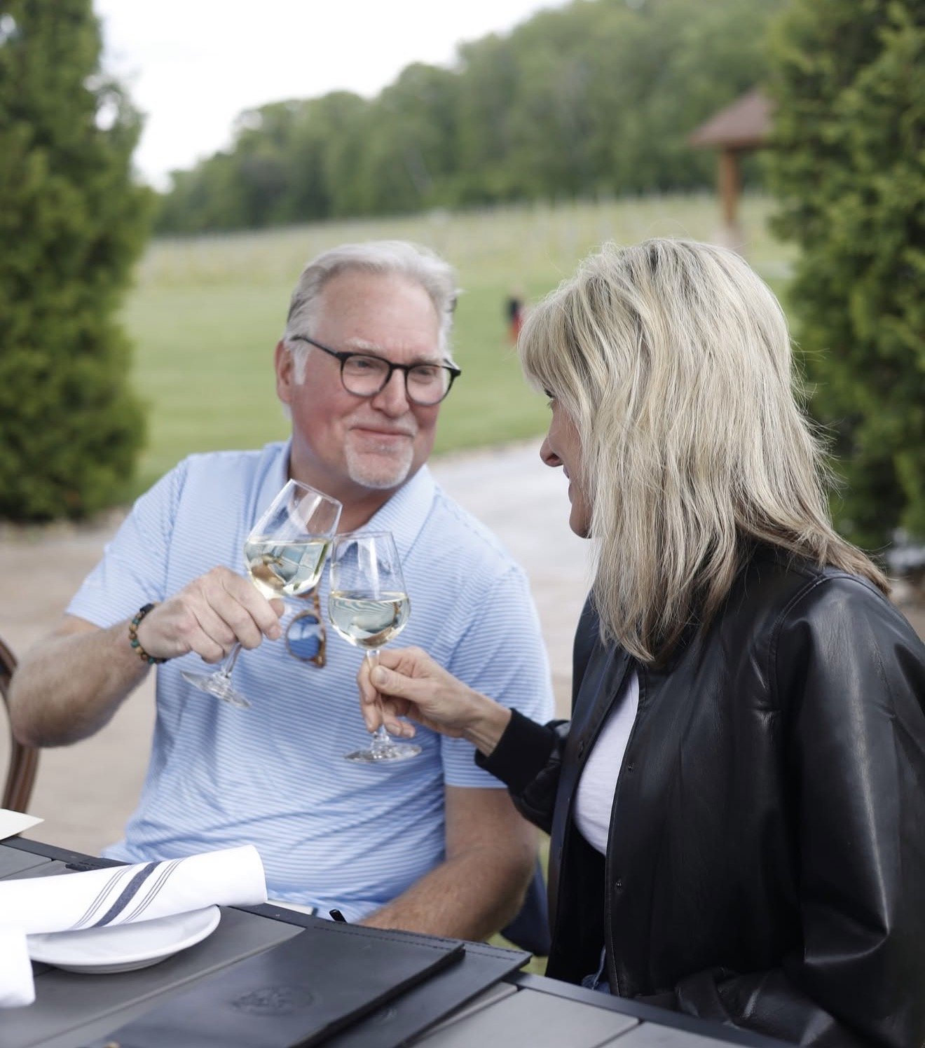 An elderly man and woman clinking glasses of white wine during an outdoor meal at a restaurant.
