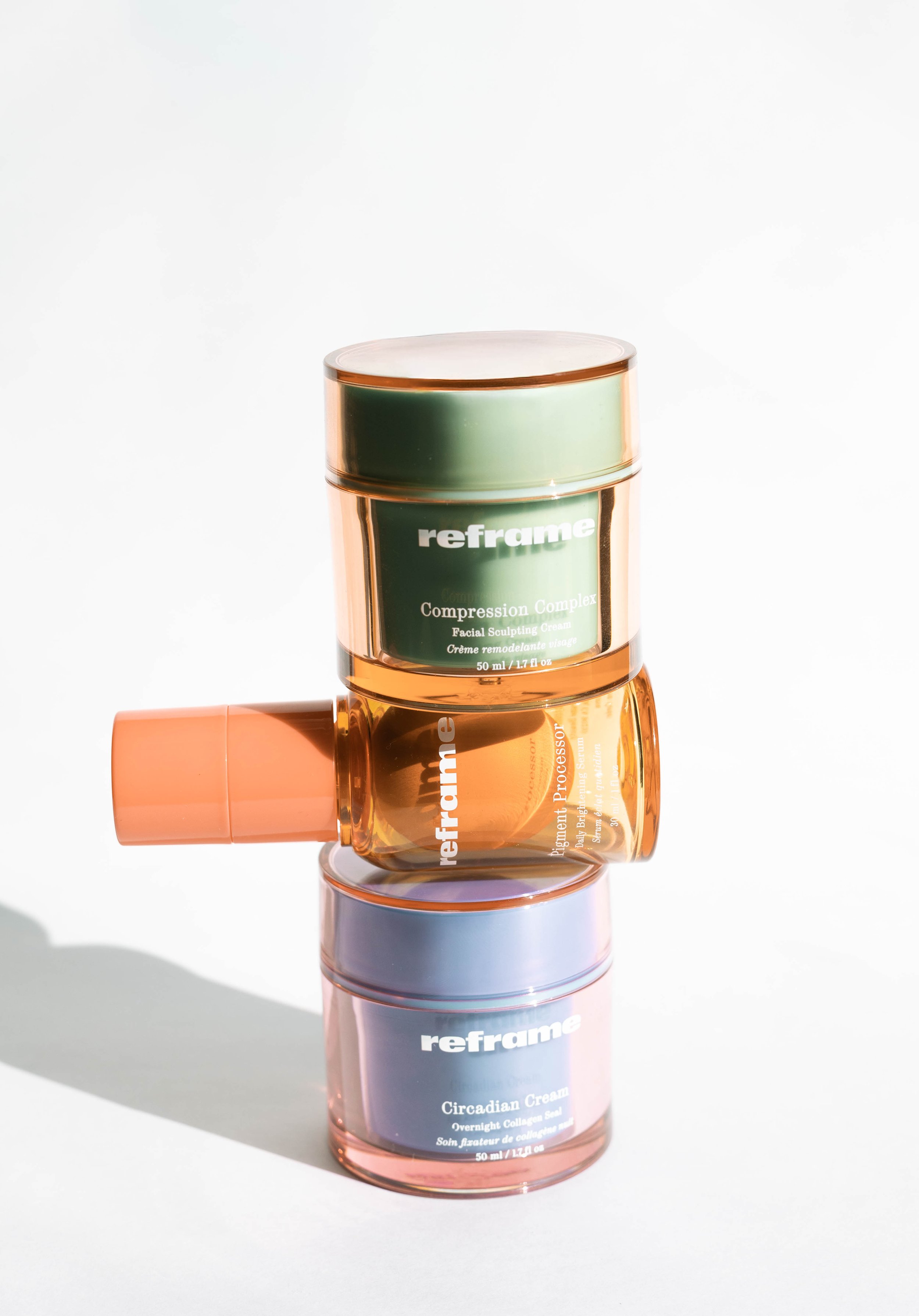Three jars of skincare cream stacked on top of each other with mirrored reflections on a white surface, with a white background.