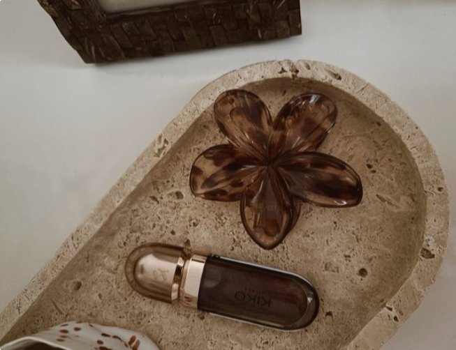 A decorative brown glass flower and a small perfume bottle on a beige stone surface.