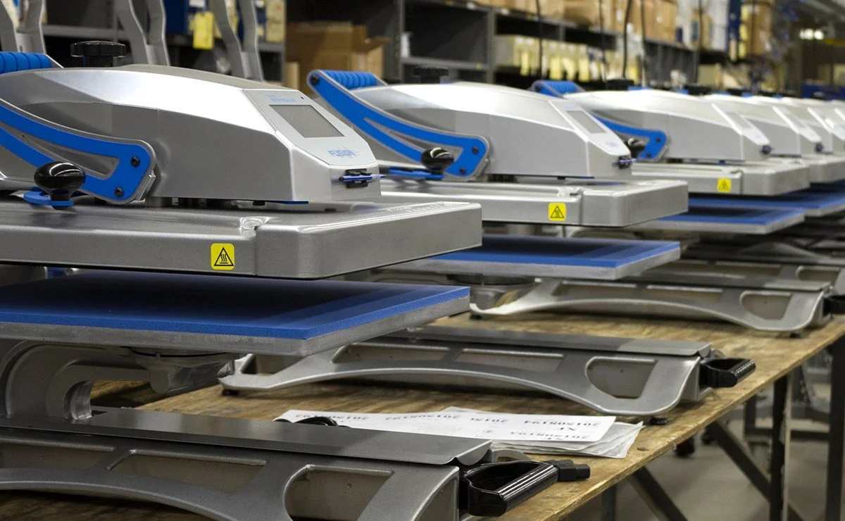 Several industrial heat press machines lined up on a workbench in a workshop or warehouse.