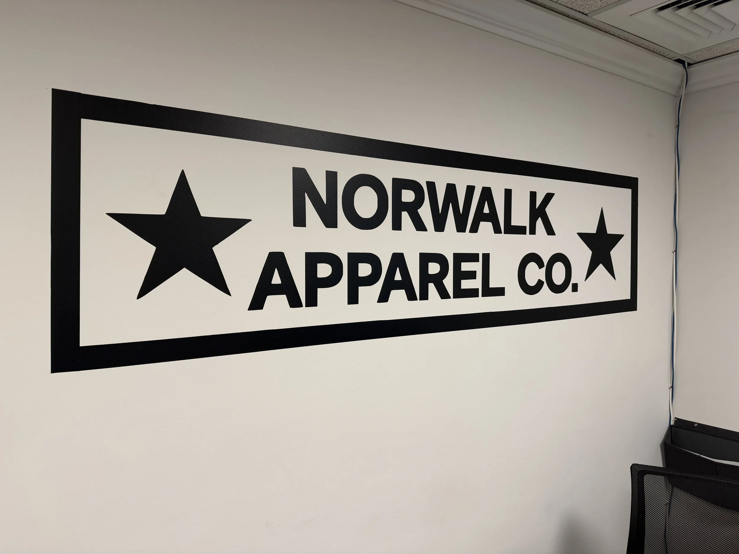 Wall sign for Norwalk Apparel Co. featuring black stars and black text on a white background.
