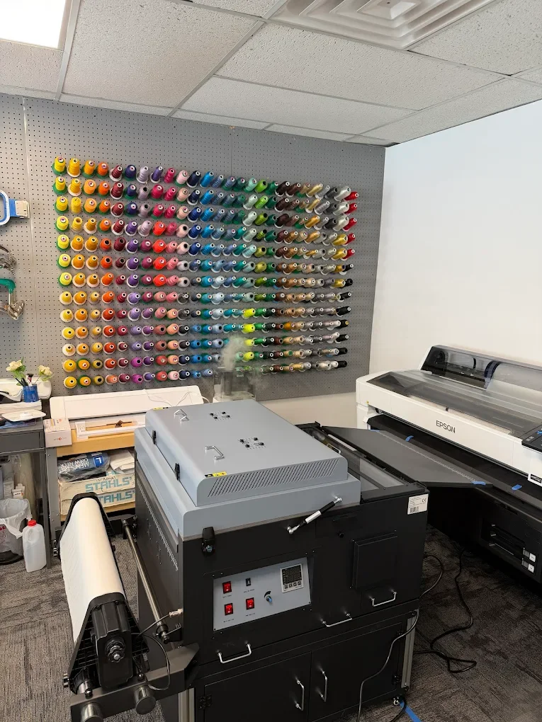 Office craft room with wall-mounted colorful spools of thread, a large Epson inkjet printer, a laminator, and other office supplies.