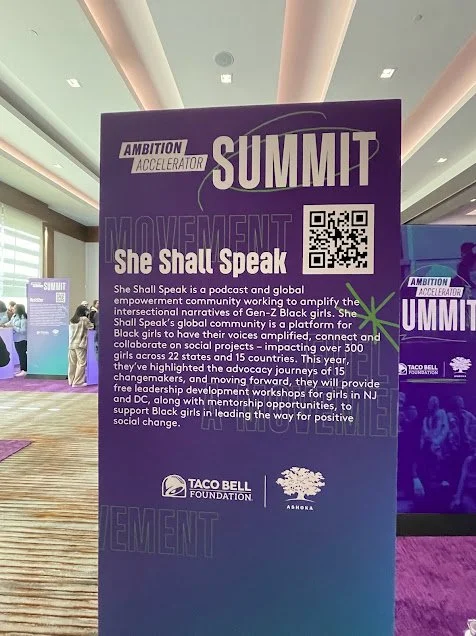Purple informational sign for the ambition accelerator summit titled "She Shall Speak". Includes a QR code, logos of Taco Bell Foundation and Ashoka, and descriptive text about the podcast and community for Black girls.