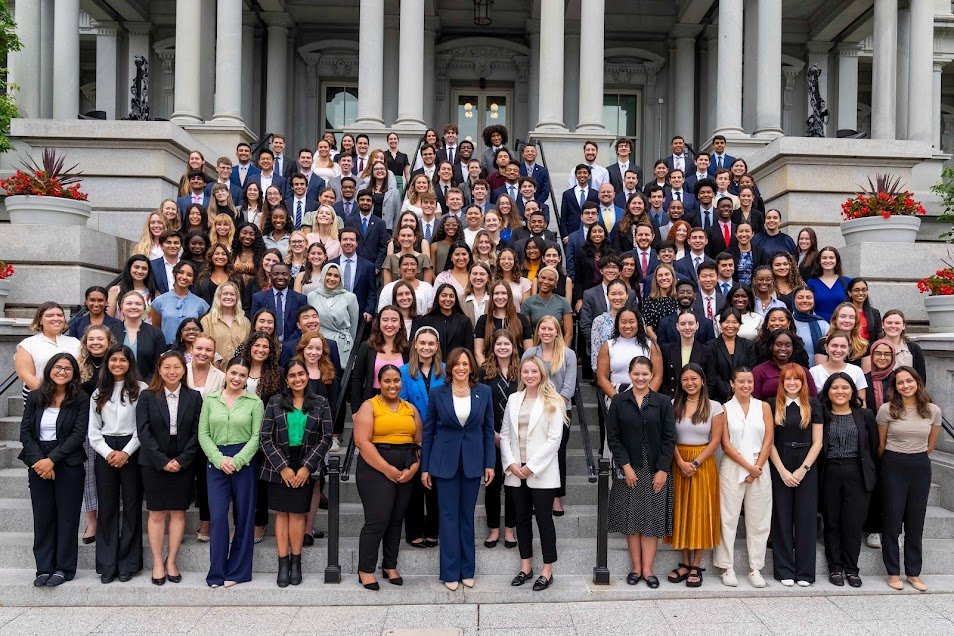 A large diverse group of women in professional attire standing on the steps of a government building, posing for a group photo.