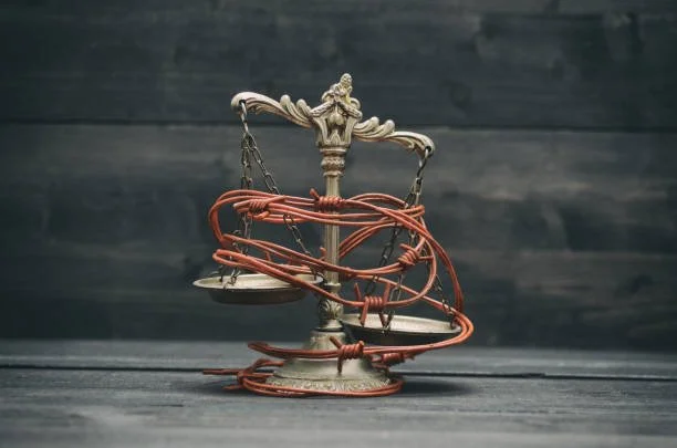 Oldish courtroom scale with tangled red wire and lock, set against a dark wooden background.