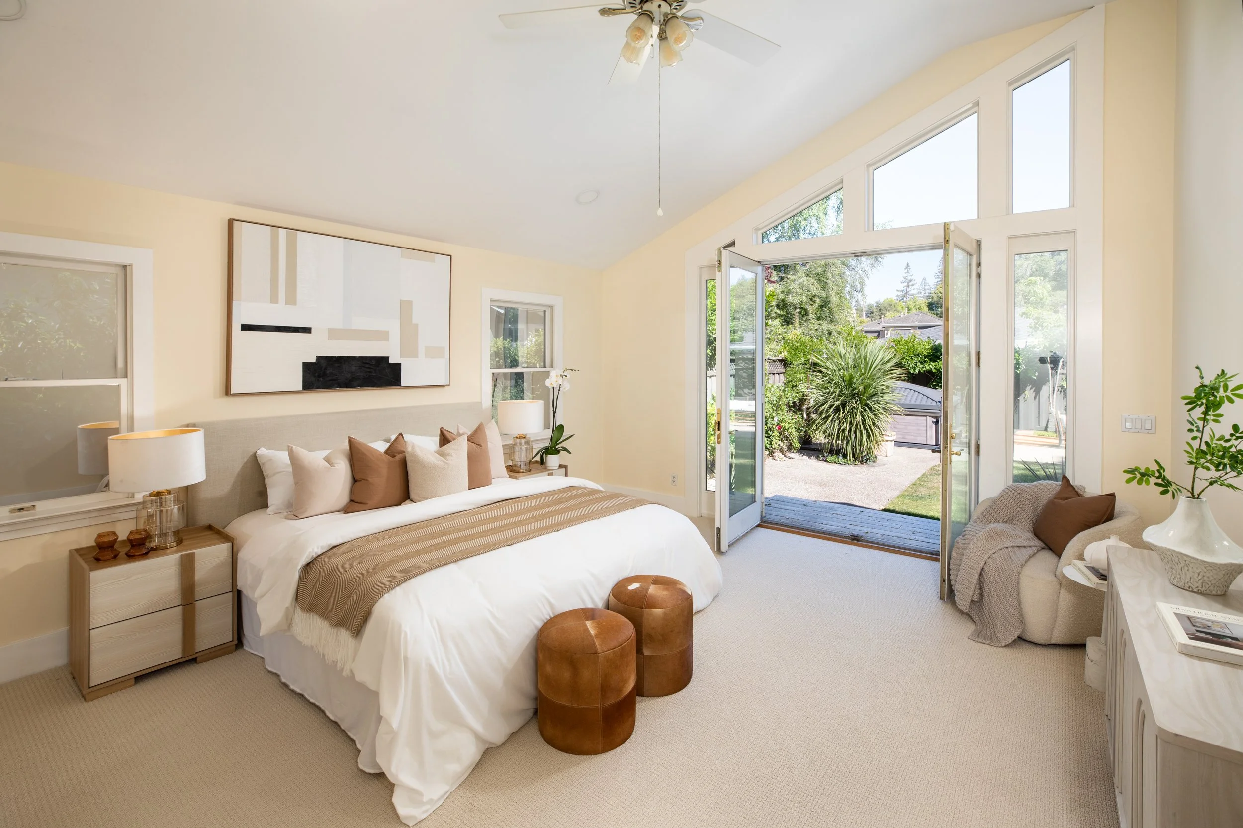 A bedroom with a bed, side tables, lamps, and a large window open to a garden outside.