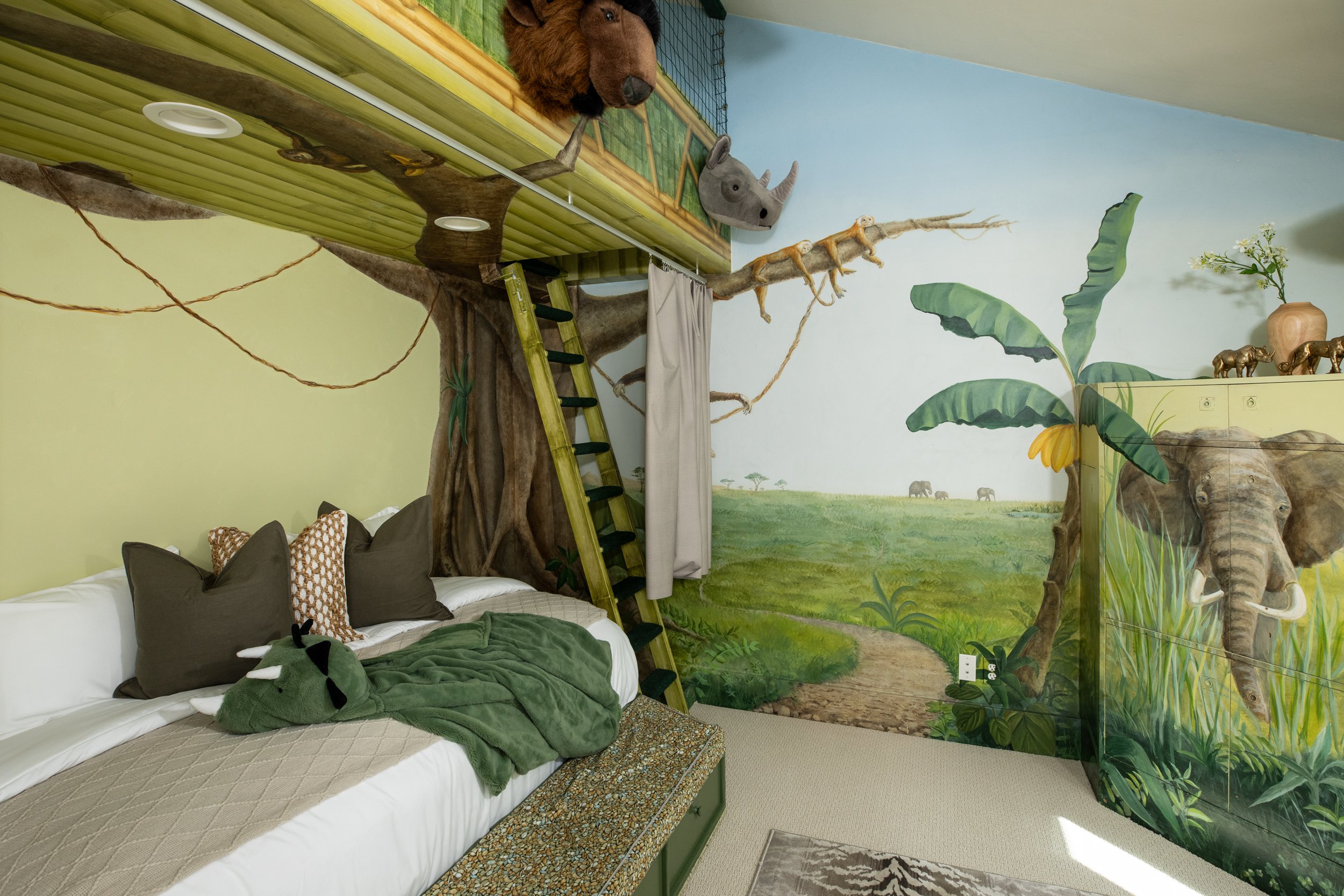 A bedroom with jungle-themed decor, including a mural of grassland animals, a tree structure with a platform and ladder, soft bedding with animal plush toys, and decorative pillows.