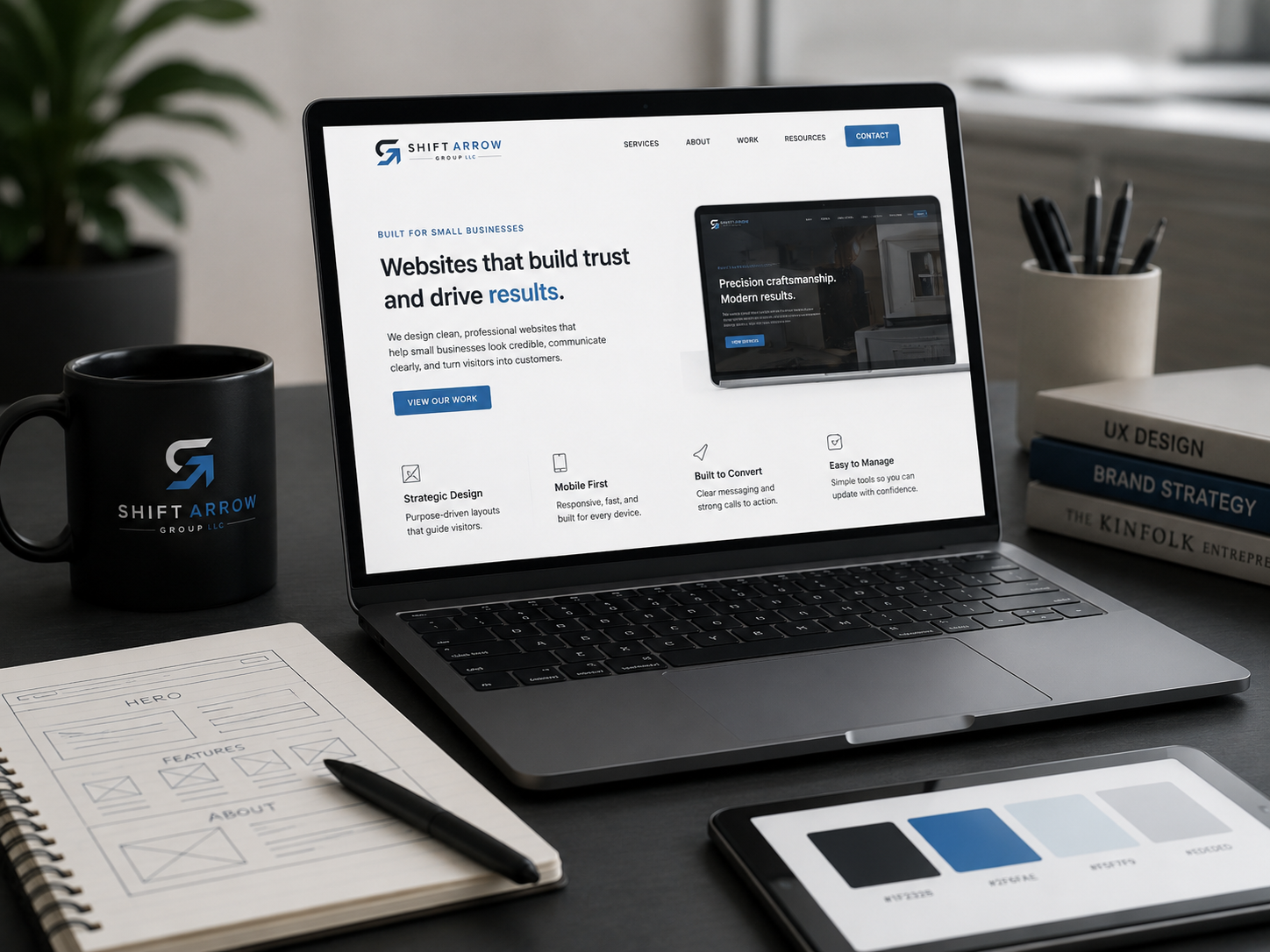 Laptop displaying the Shift Arrow Group website with branding and website design materials on a desk.