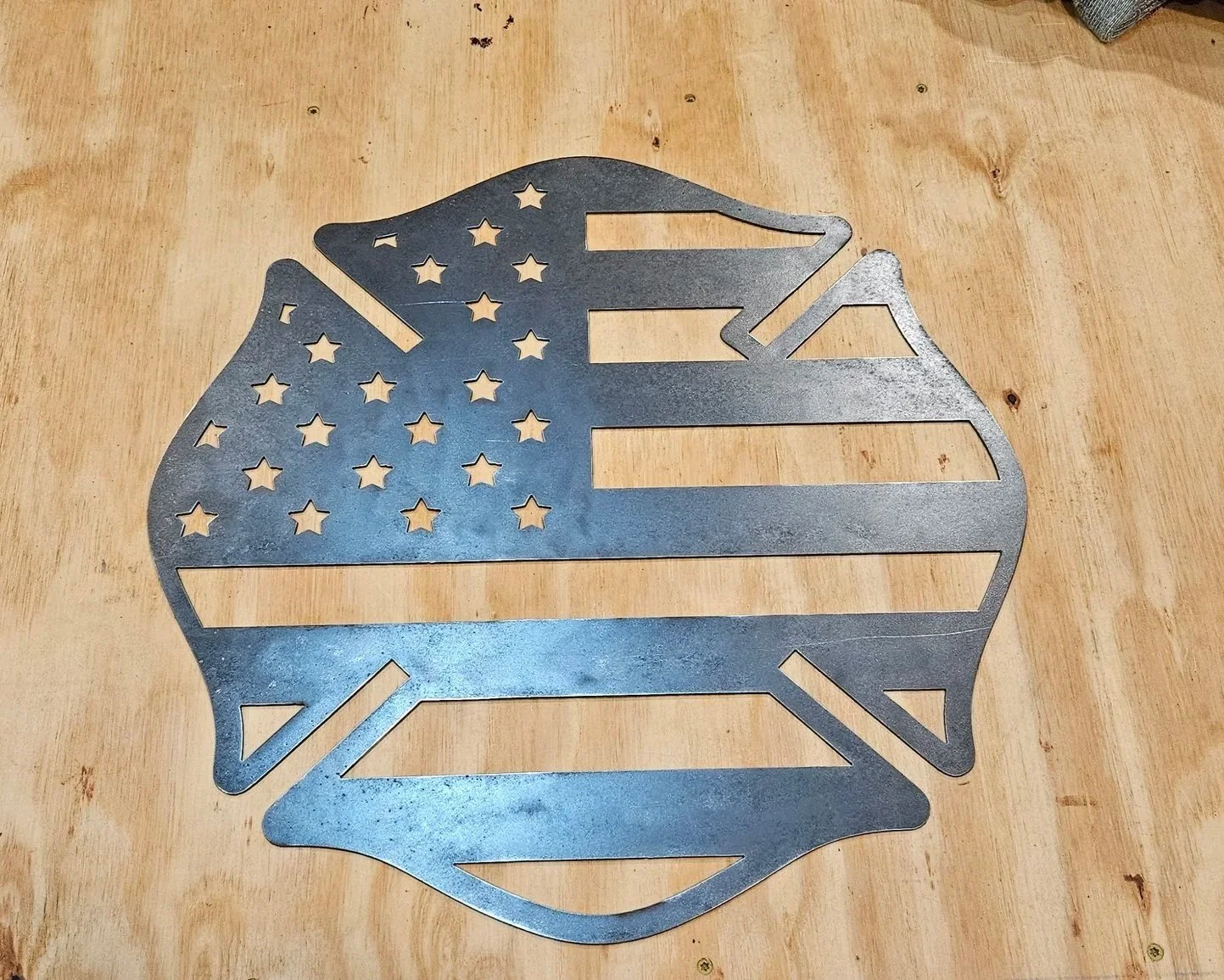 A metal cutout of a Maltese cross designed with the pattern of the American flag, placed on a wooden surface.