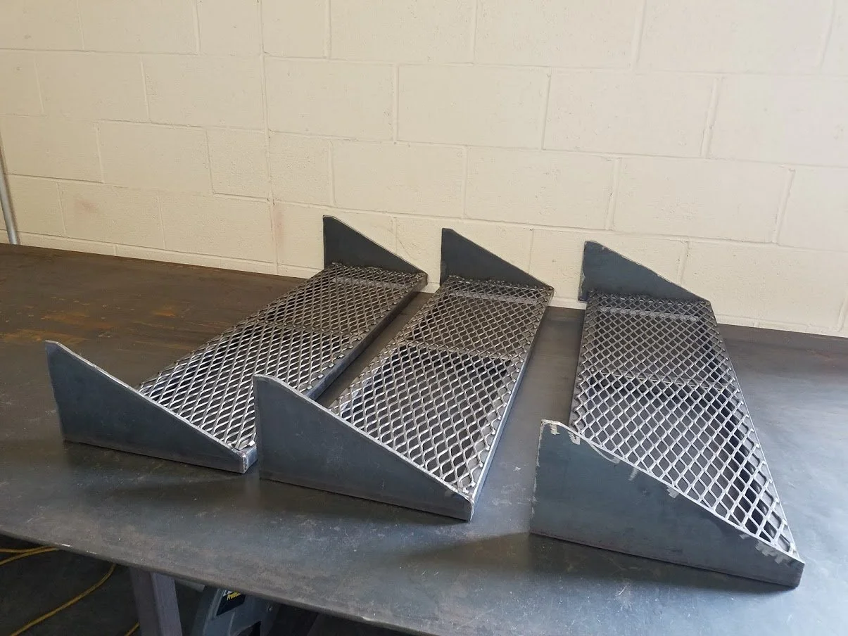 Three metal wedge-shaped metal grates with mesh tops, placed side by side on a black work surface.