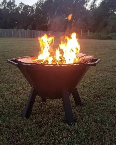 A metal fire pit with flames on a grassy lawn in a backyard.