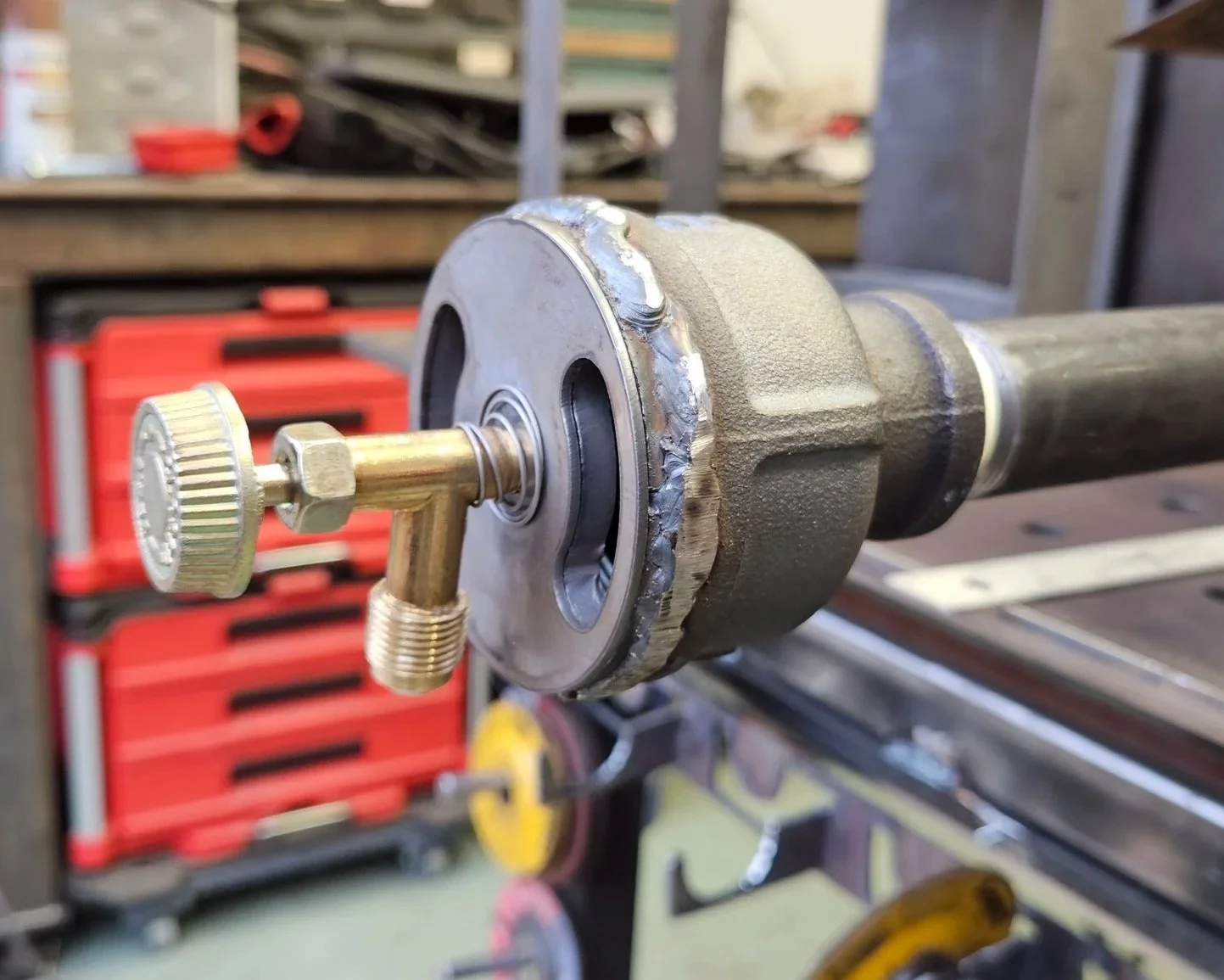 Close-up of a mechanical part with a gear and threaded bolt, mounted on a metal shaft in a workshop setting.
