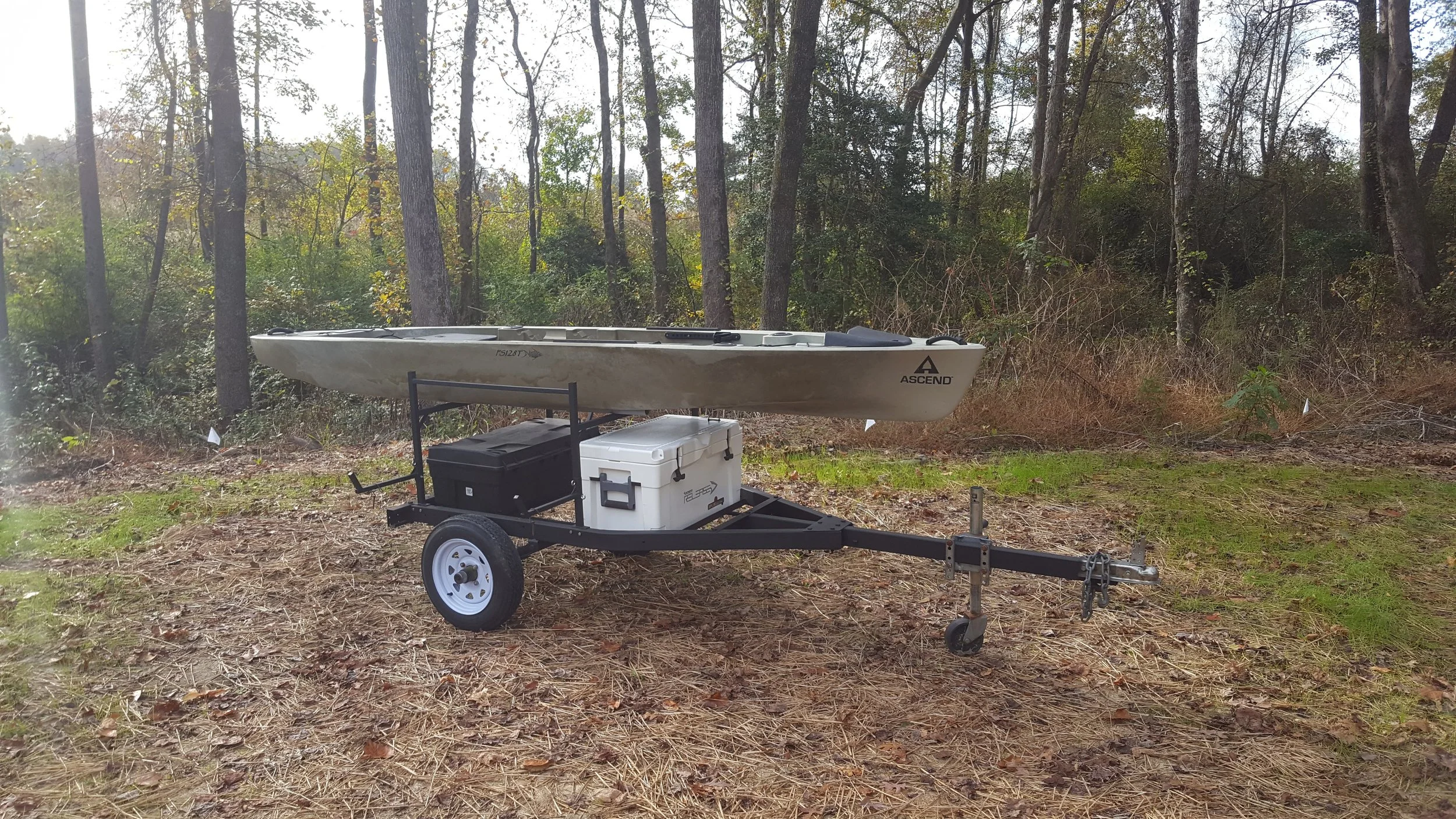 A kayak on a trailer in a wooded area with tall trees and green foliage.