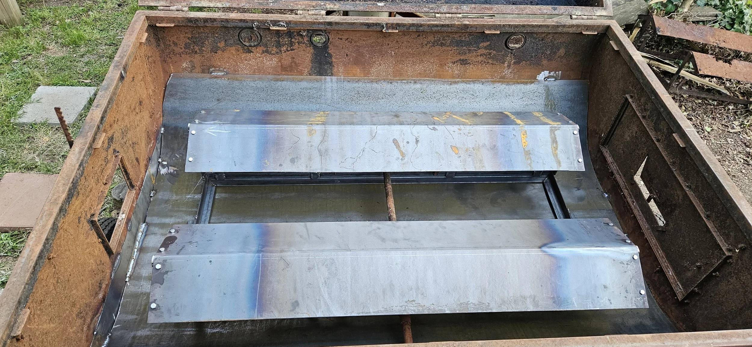 The interior of an old rusted metal grill with new shiny metal plates installed in the bottom.