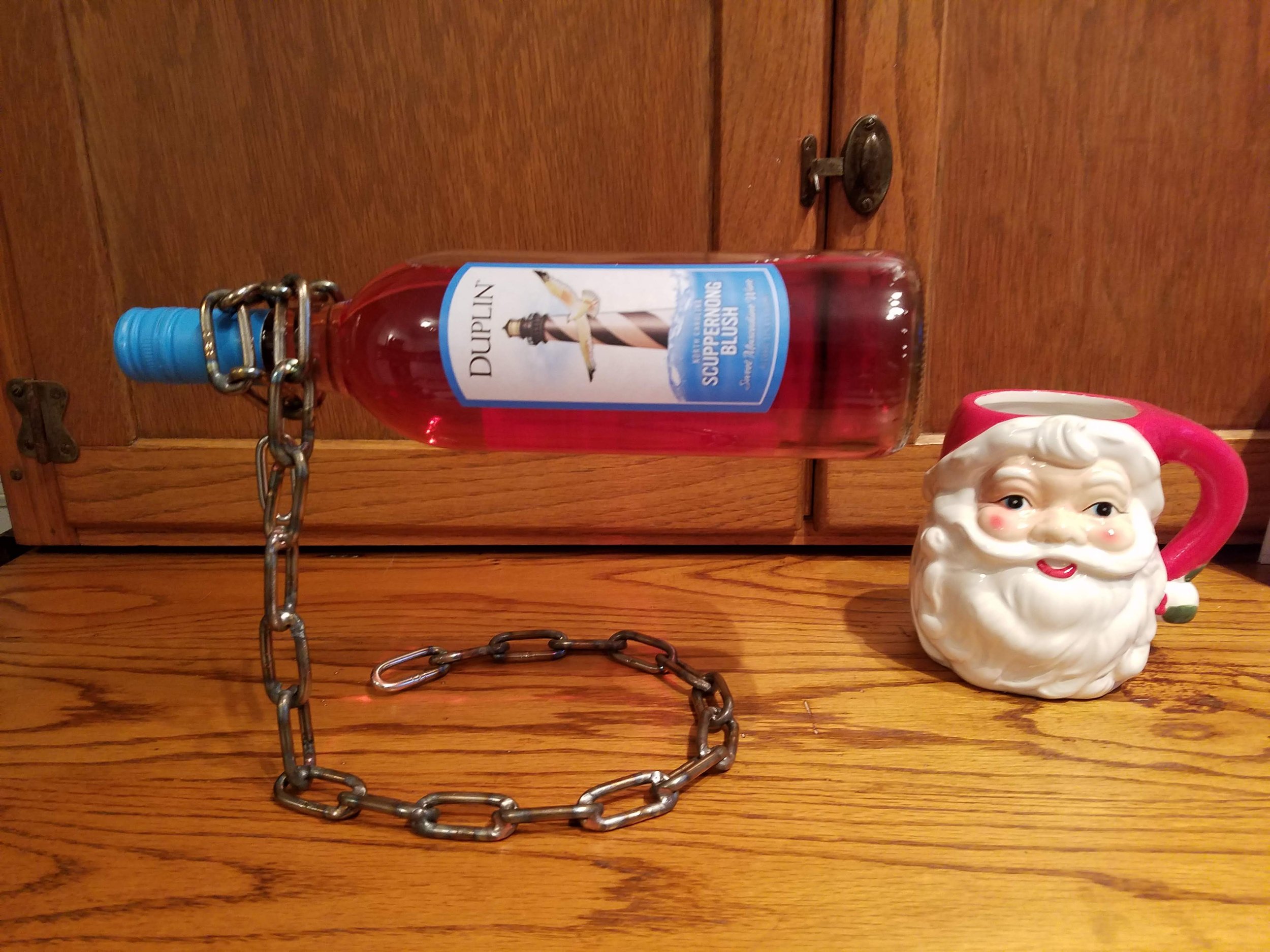 A wooden cabinet with a Santa Claus mug, a Santa-themed bottle of syrup, and a chain in front of it.