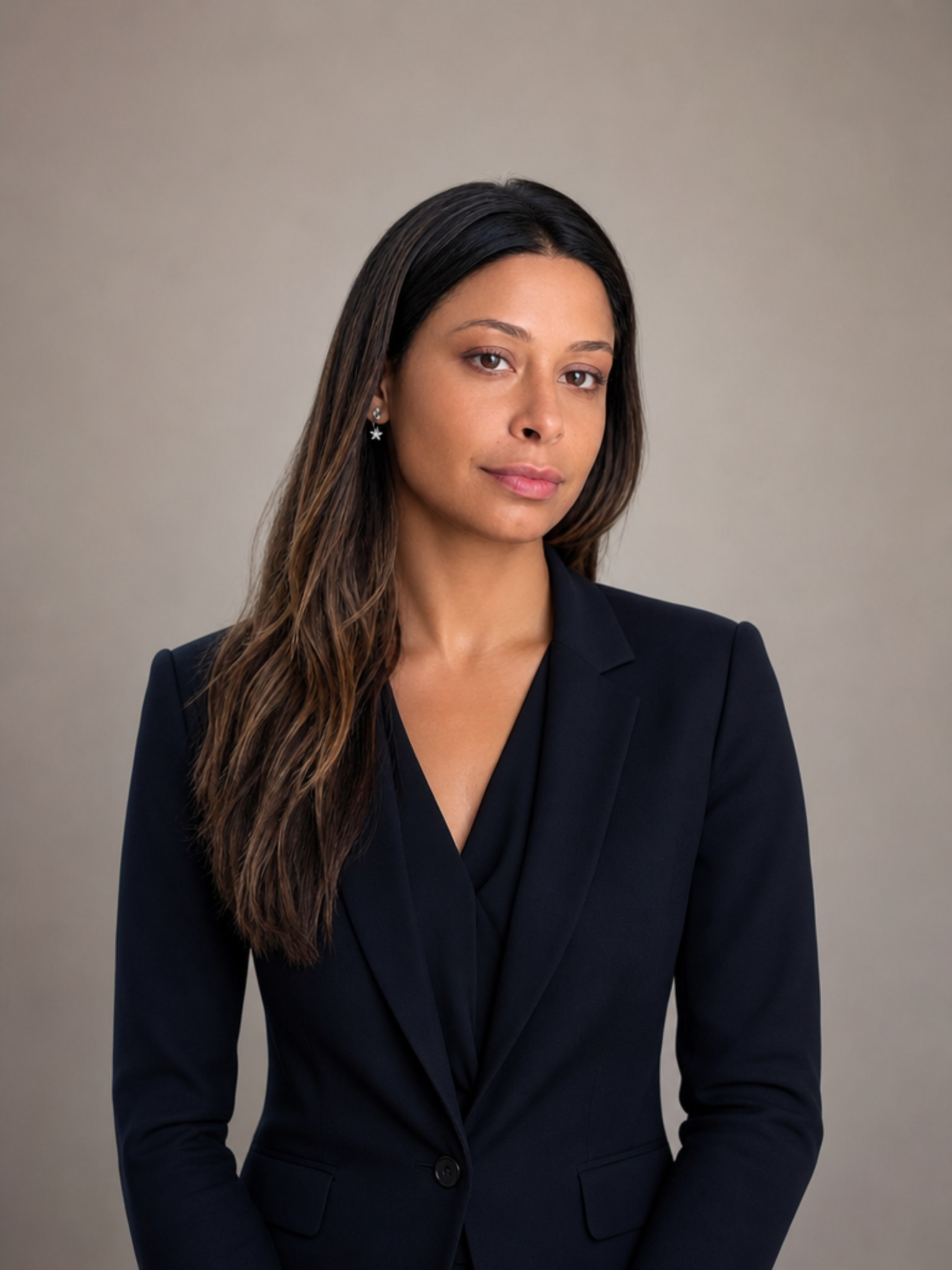 Portrait d'une avocate d'âge adulte portant un tailleur noir, sur un fond gris neutre.