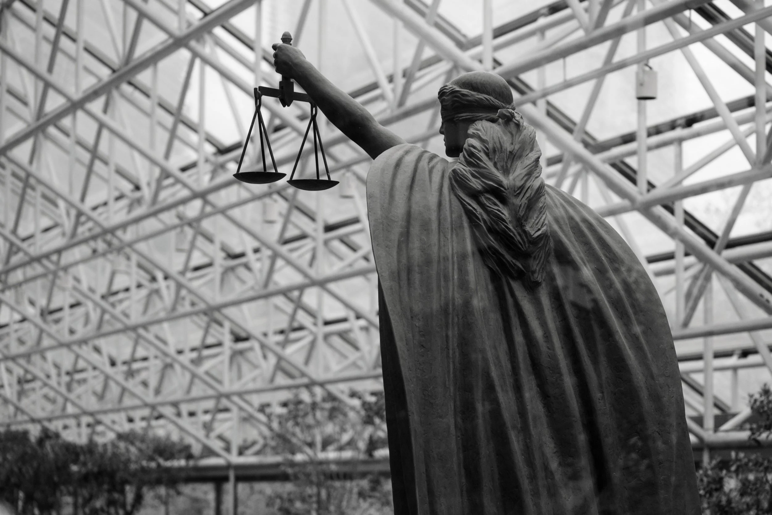 Statue de la Déclaration de la liberté avec une balance à la main, vue de dos, dans un bâtiment avec une structure en métal au plafond.