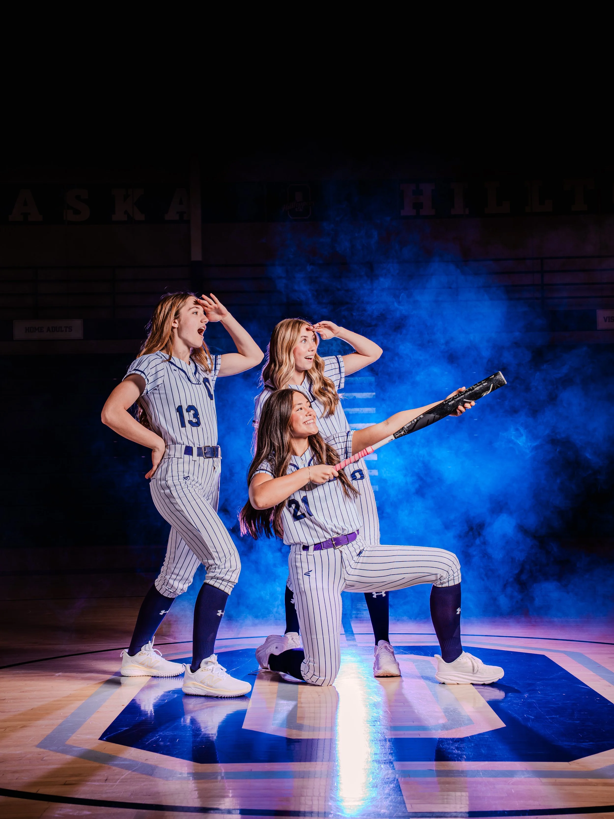 Four young women in striped sports uniforms perform a choreographed pose on a basketball court, with a blue smoky background and the words 'ASKA' and 'HILLT' visible in the background.