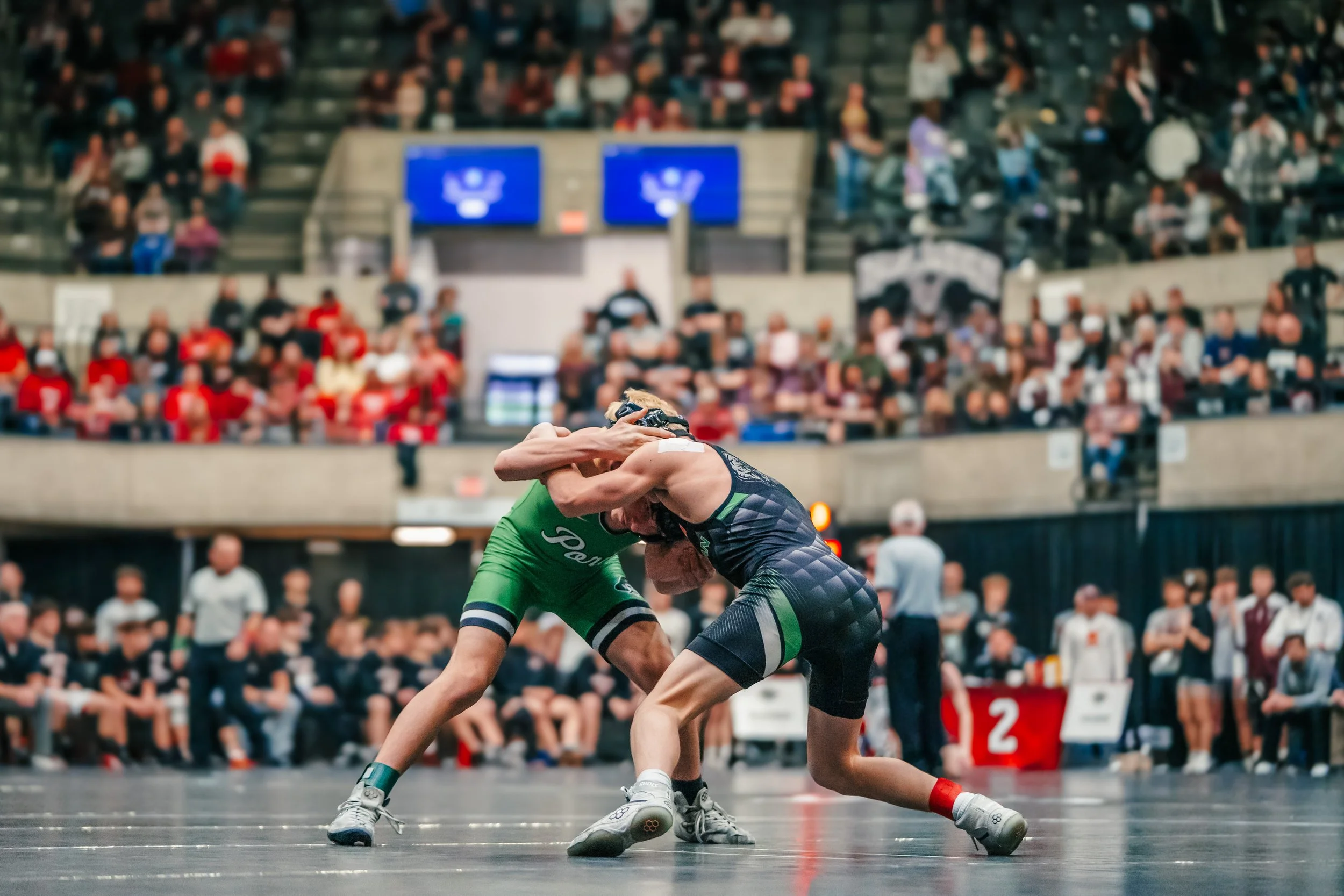 Two wrestlers competing on a mat during a wrestling match in front of an audience in a gymnasium.
