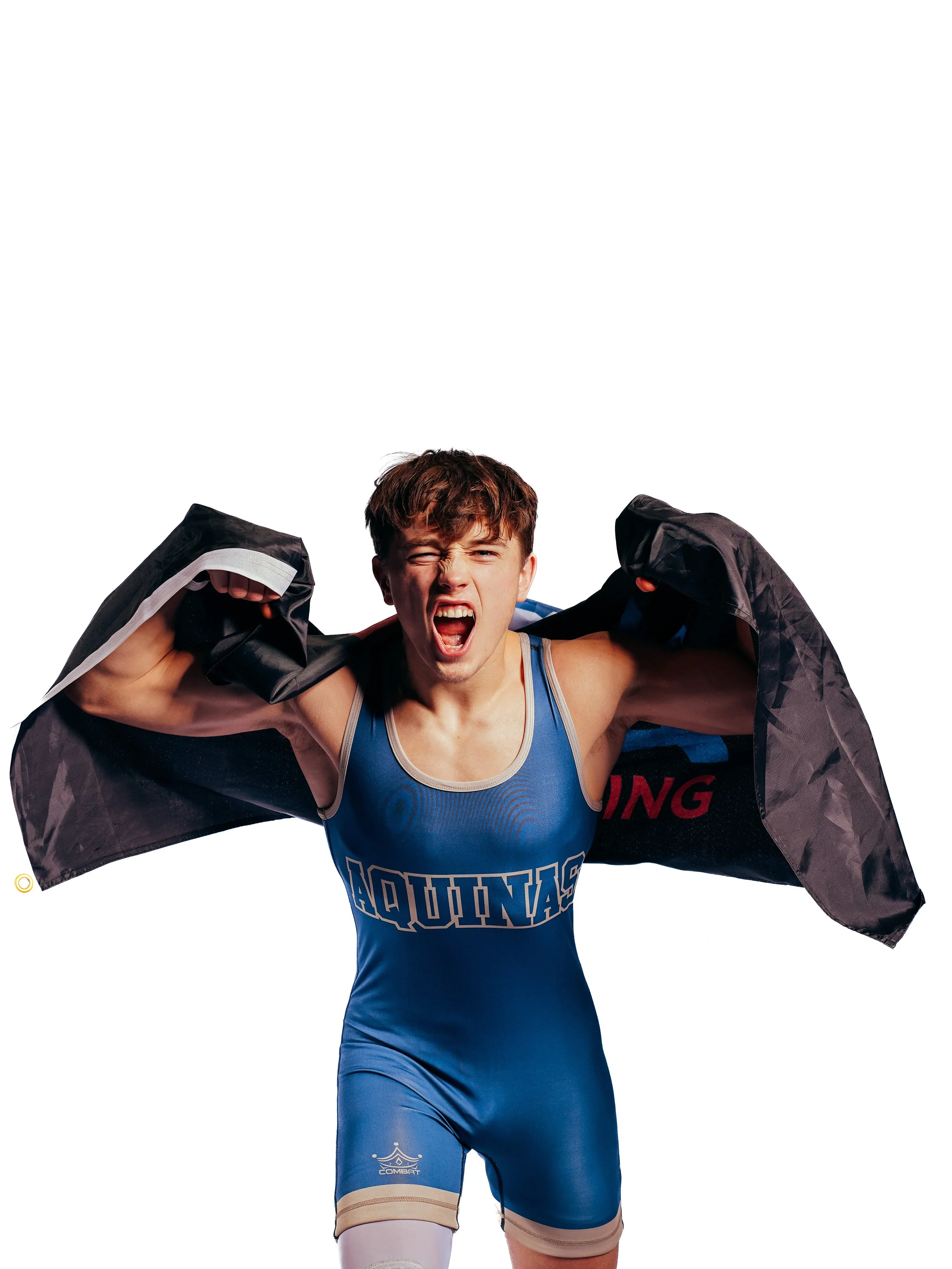 A male athlete in a blue wrestling singlet with the word 'AQUINAS' on it, pulling off a jacket, with a facial expression of exertion or shouting, white background.