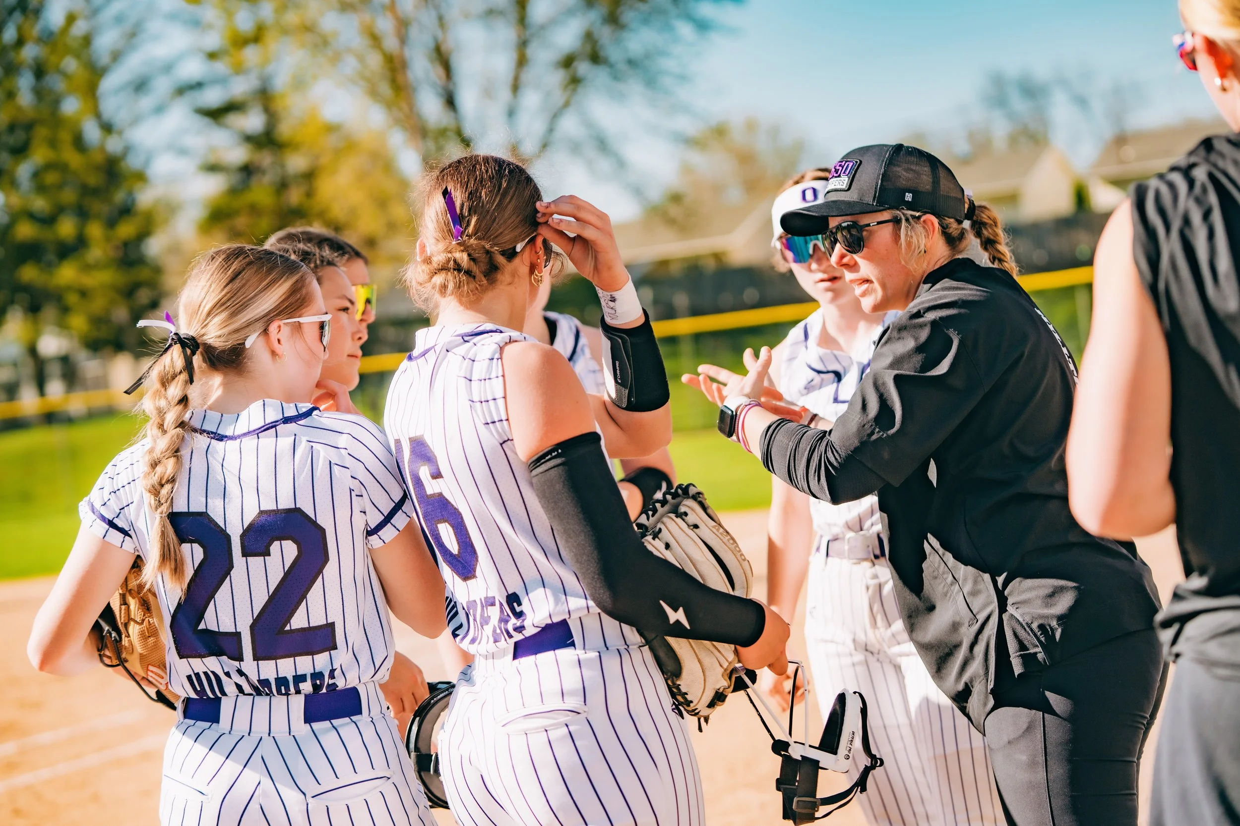 Softball players in striped uniforms talking to a coach or umpire on the field during daytime.