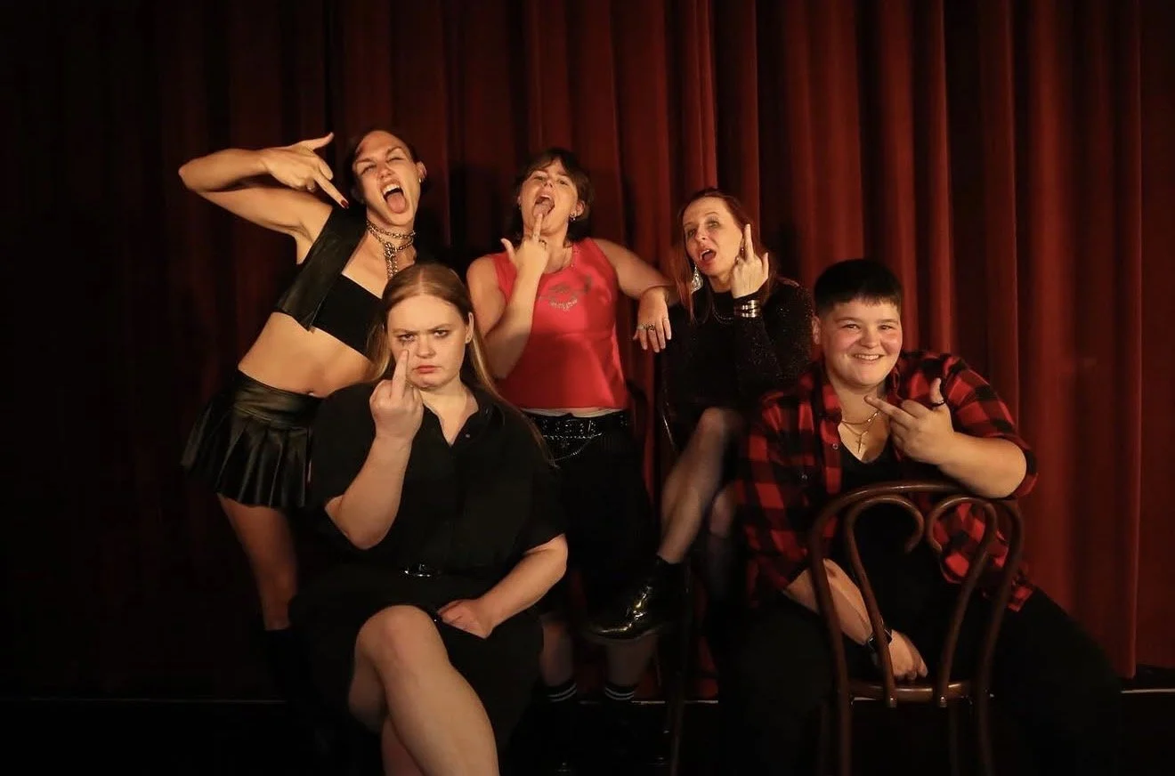 Five young people posing in front of red curtains, making expressive gestures and faces, some showing middle fingers, in a lively and rebellious atmosphere.