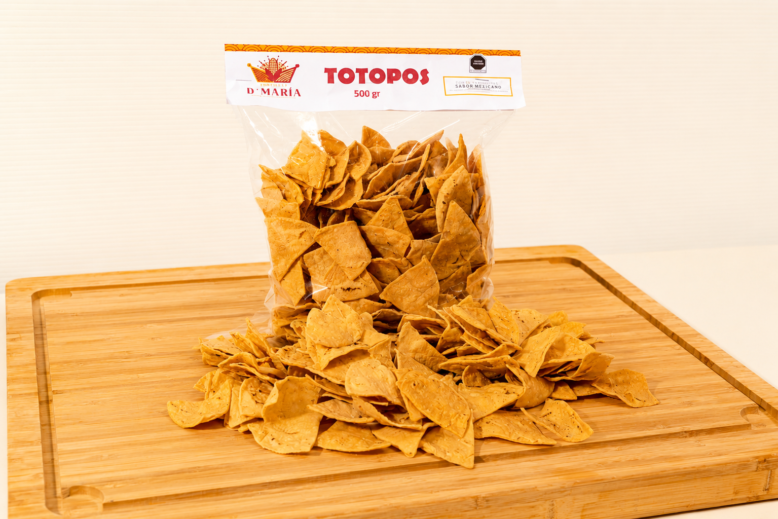 A clear plastic bag of tortilla chips labeled "Totopos 500 g" on a wooden cutting board.