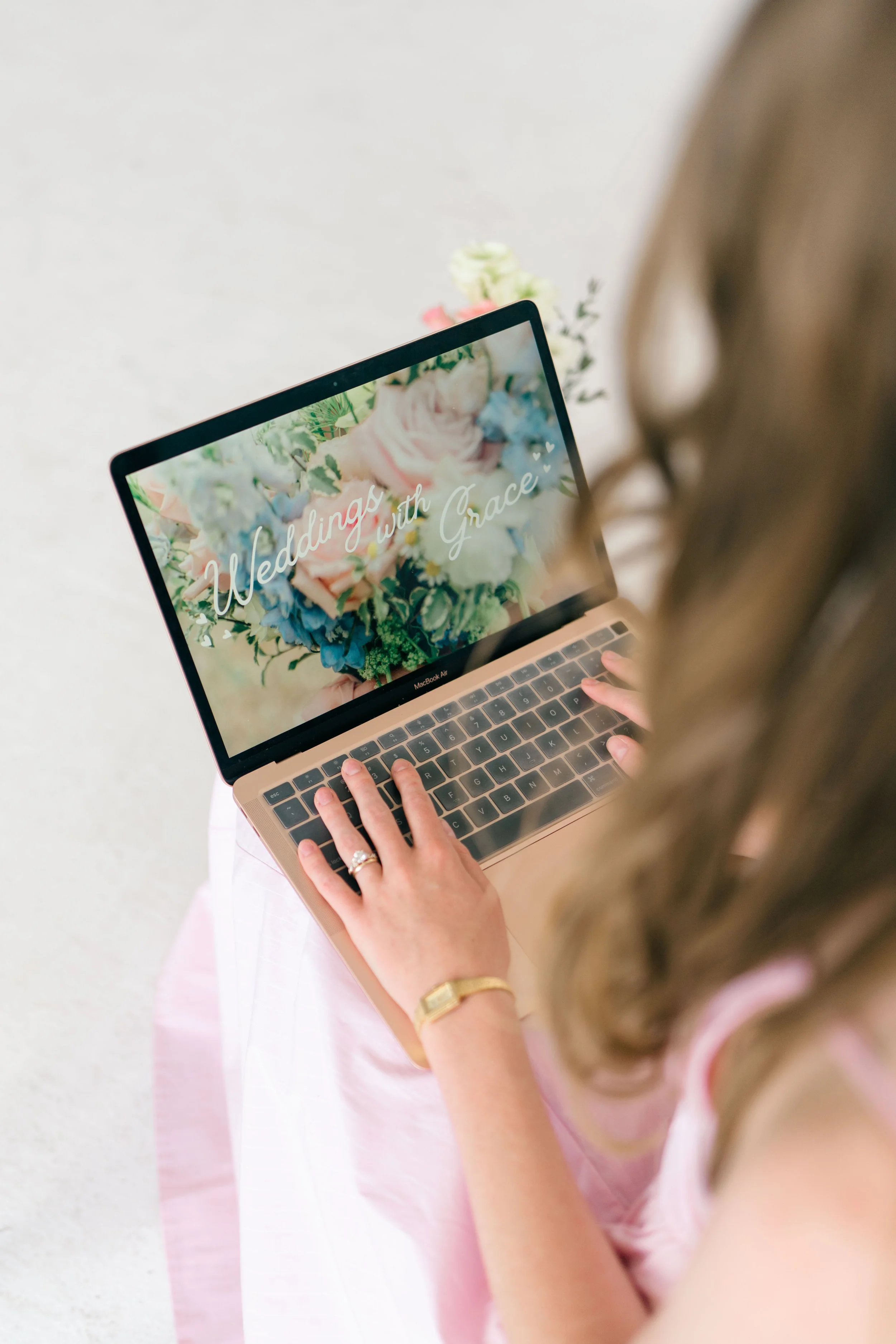 Grace Veazey typing on a laptop that displays a floral background with the words 'Weddings with Grace'.