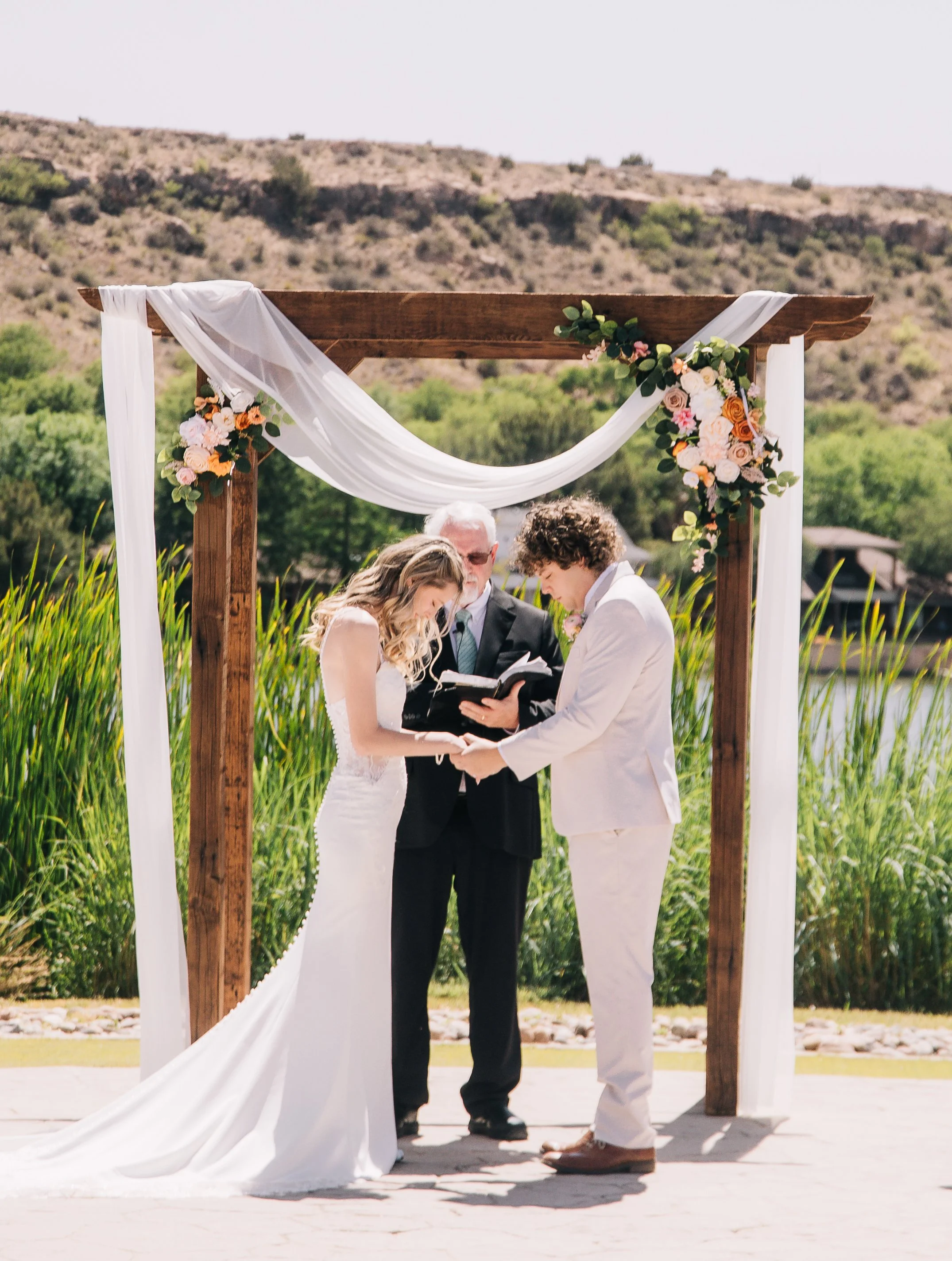Grace's clients, Kaitlyn & Luke praying under an arch with drapery and flowers at their wedding ceremony.