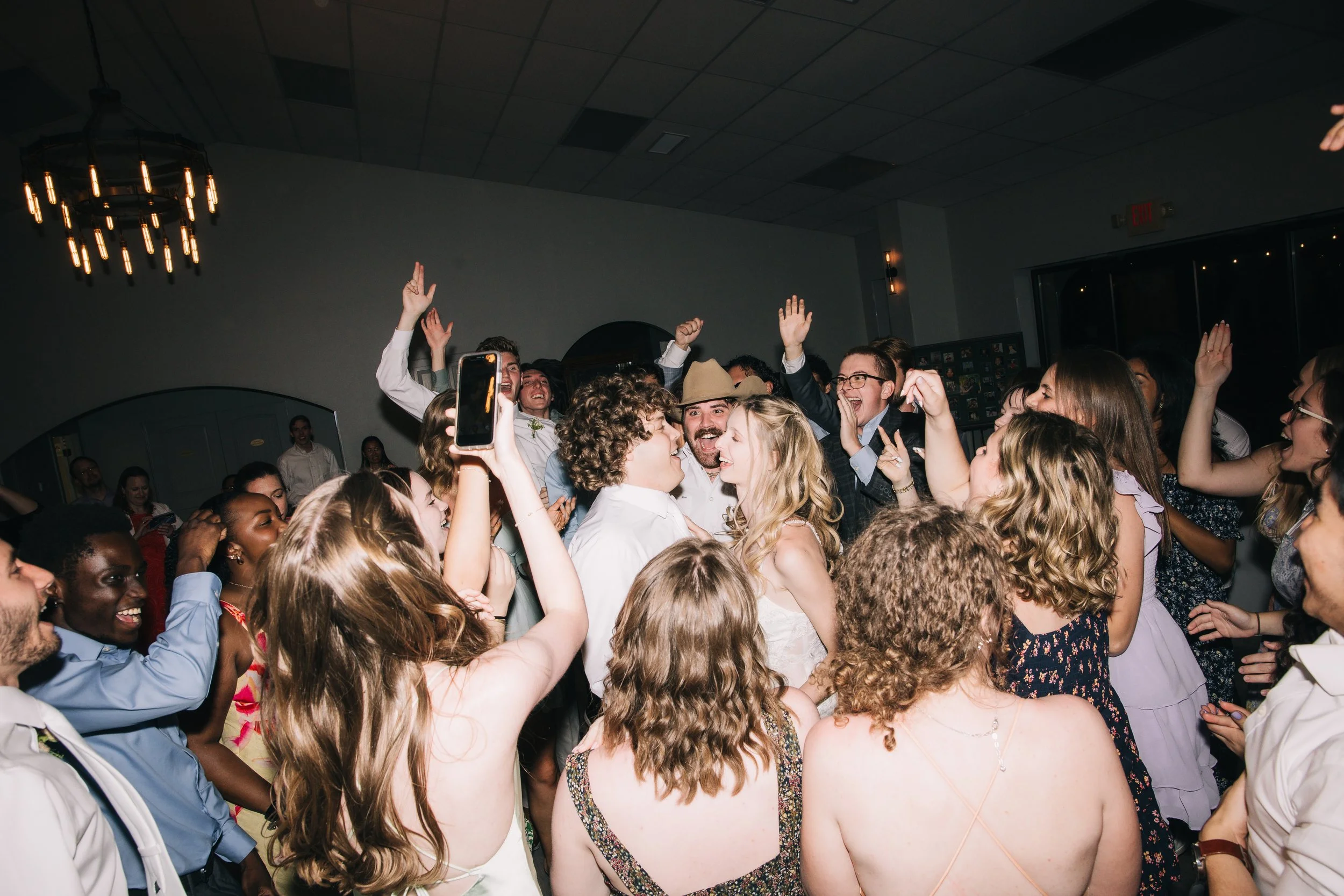Crowd of people dancing at a wedding, with some raising their hands and smiling