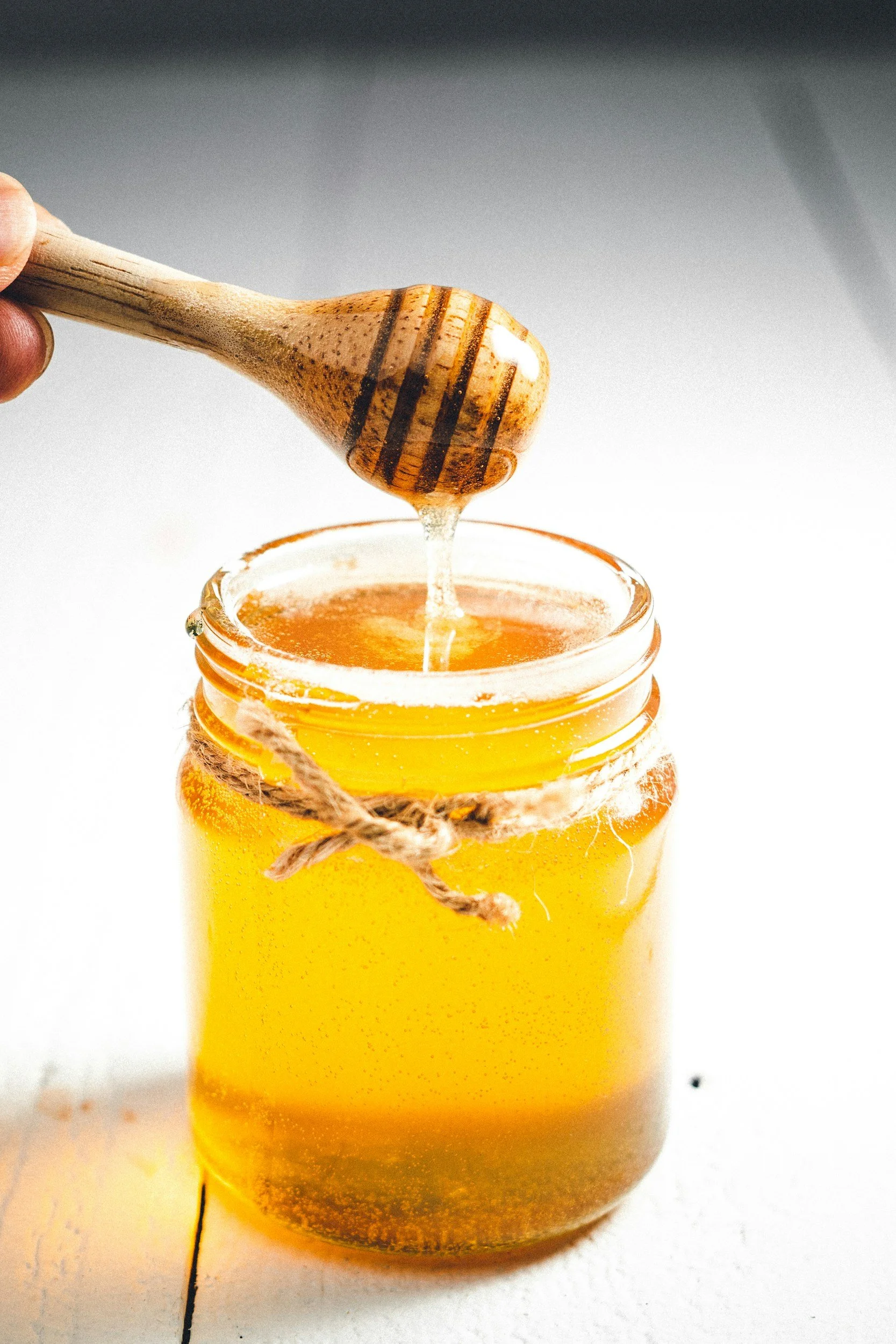 A jar of honey with a honey dipper dripping honey into the jar.