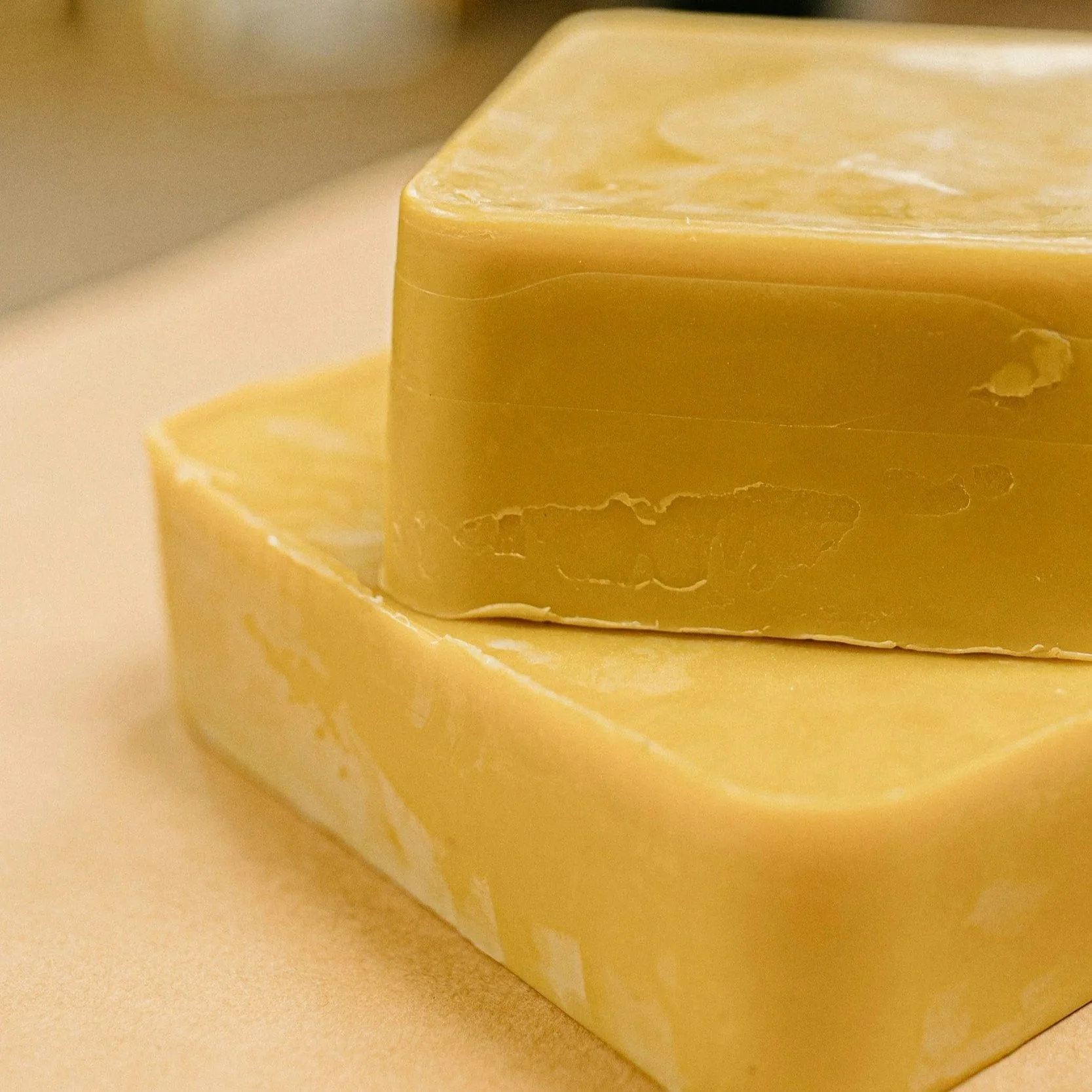 Close-up of a large bar of yellow soap with a smooth surface, resting on a beige surface.