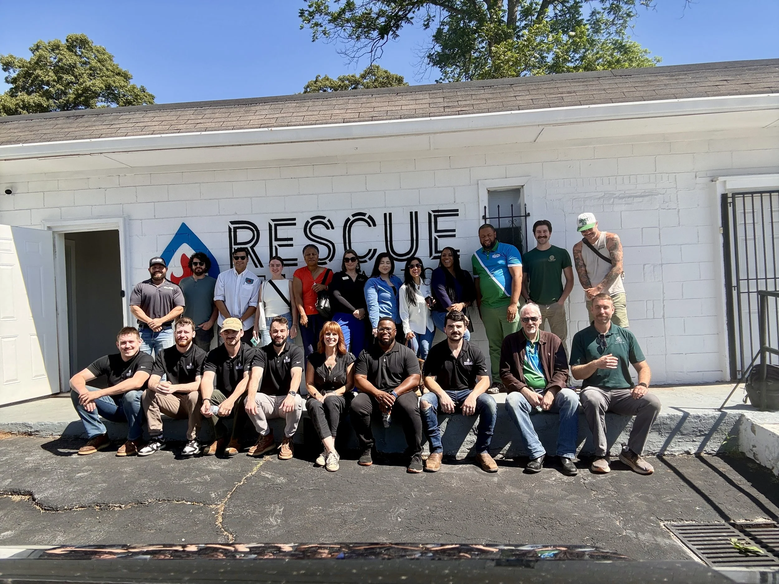 Group photo of people standing and sitting in front of a white rescue building with a blue sky background.