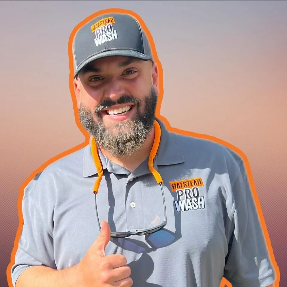 Man wearing a gray polo shirt and a black cap with the logo 'Halstead Pro Wash', smiling, giving a thumbs-up, with glasses hanging around his neck, against a gradient background.