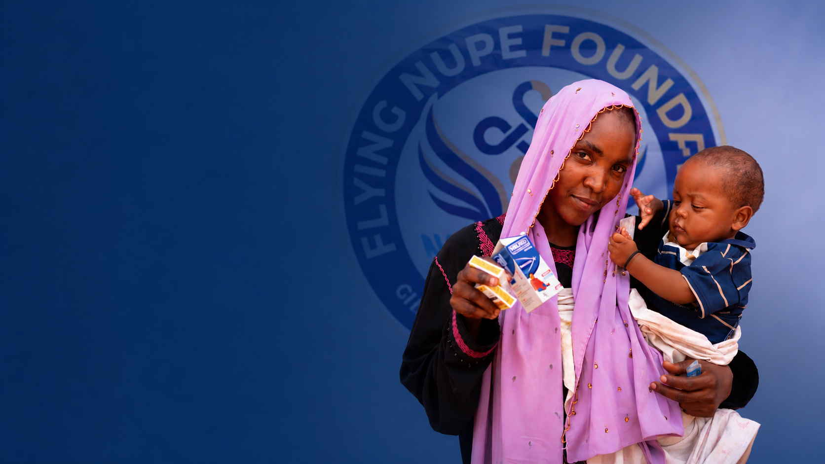 A woman wearing a purple headscarf holding a young boy dressed in a striped navy blue shirt while standing in front of a blue backdrop with the logo of the Fistula Nursing Foundation.