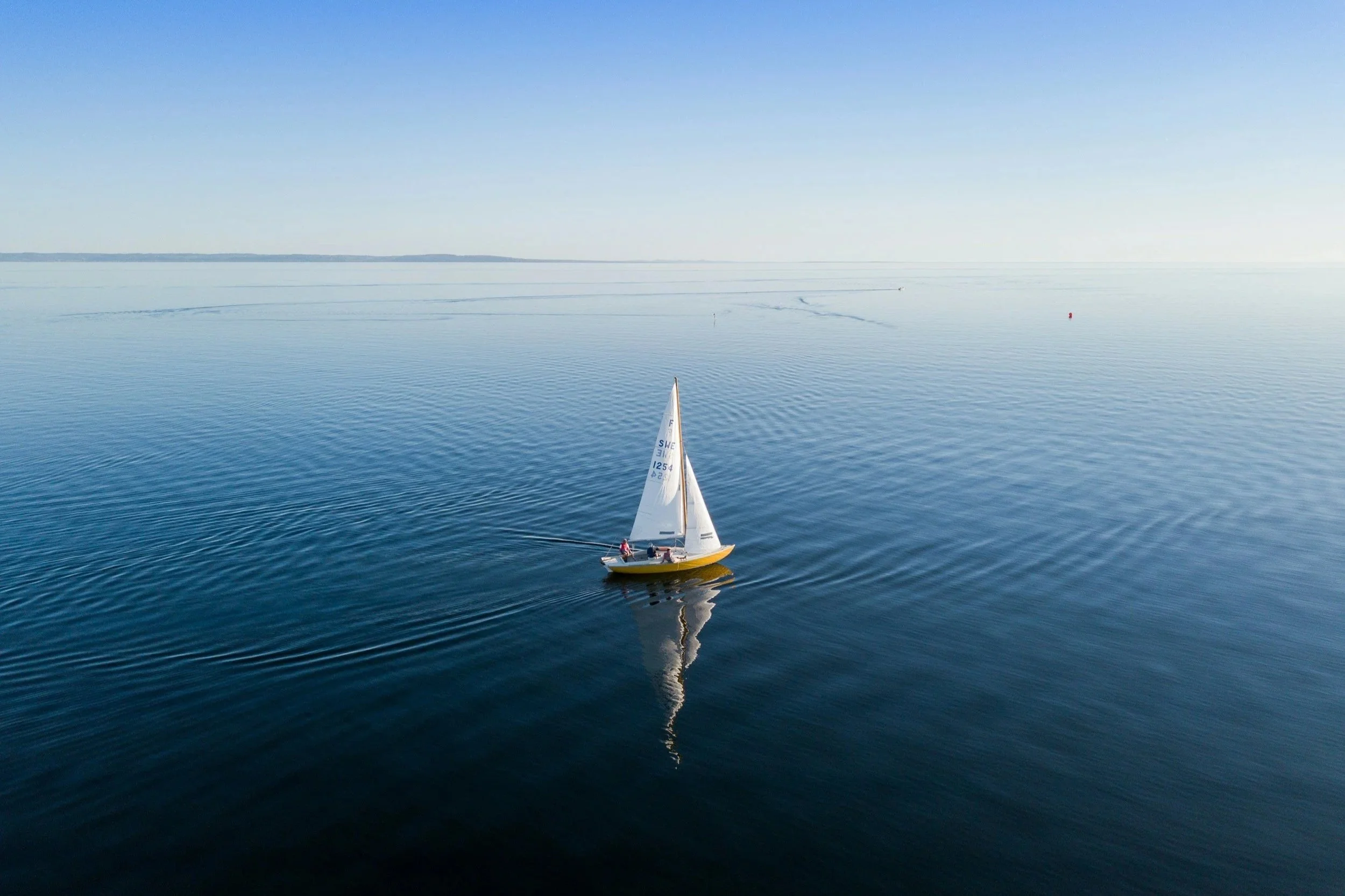 sailboat in the middle of the ocean with gradient blue coloration in the ocean