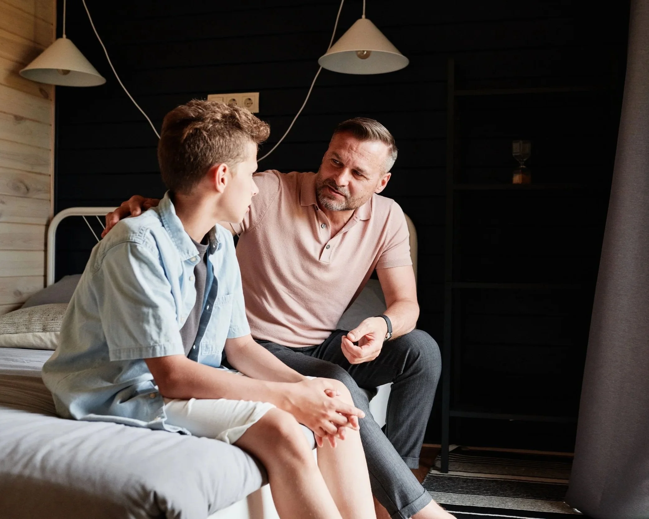 father and son sitting together talking on a bed
