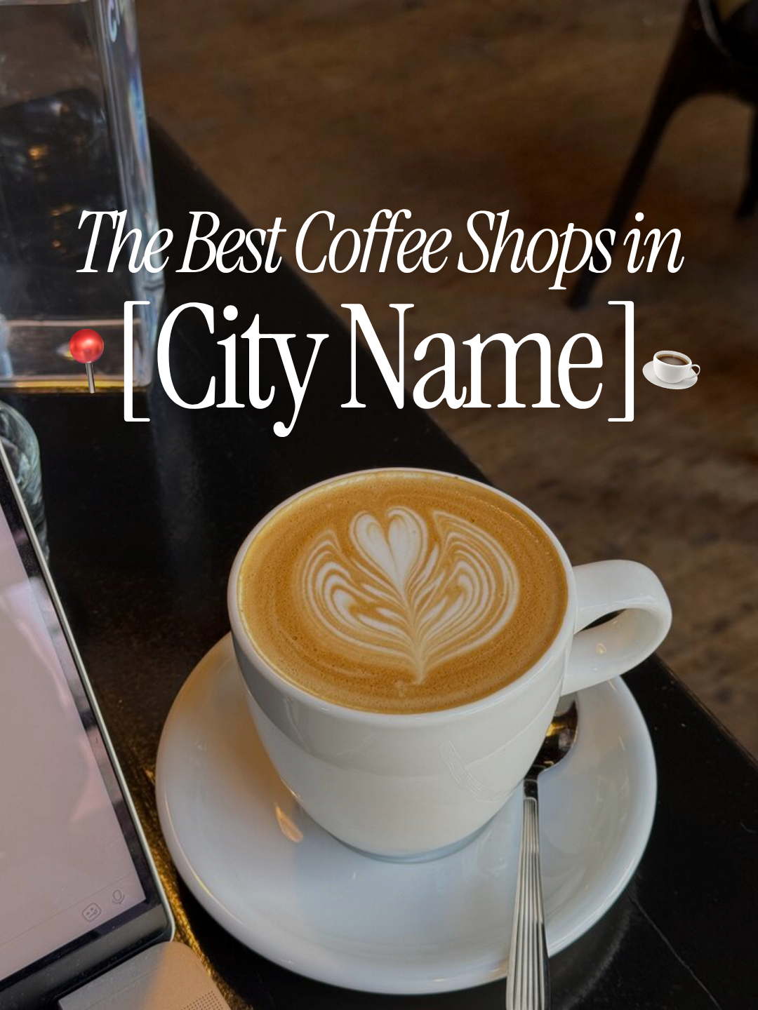 A white coffee cup with a latte art heart on top, placed on a saucer with a spoon, on a dark table in a coffee shop.