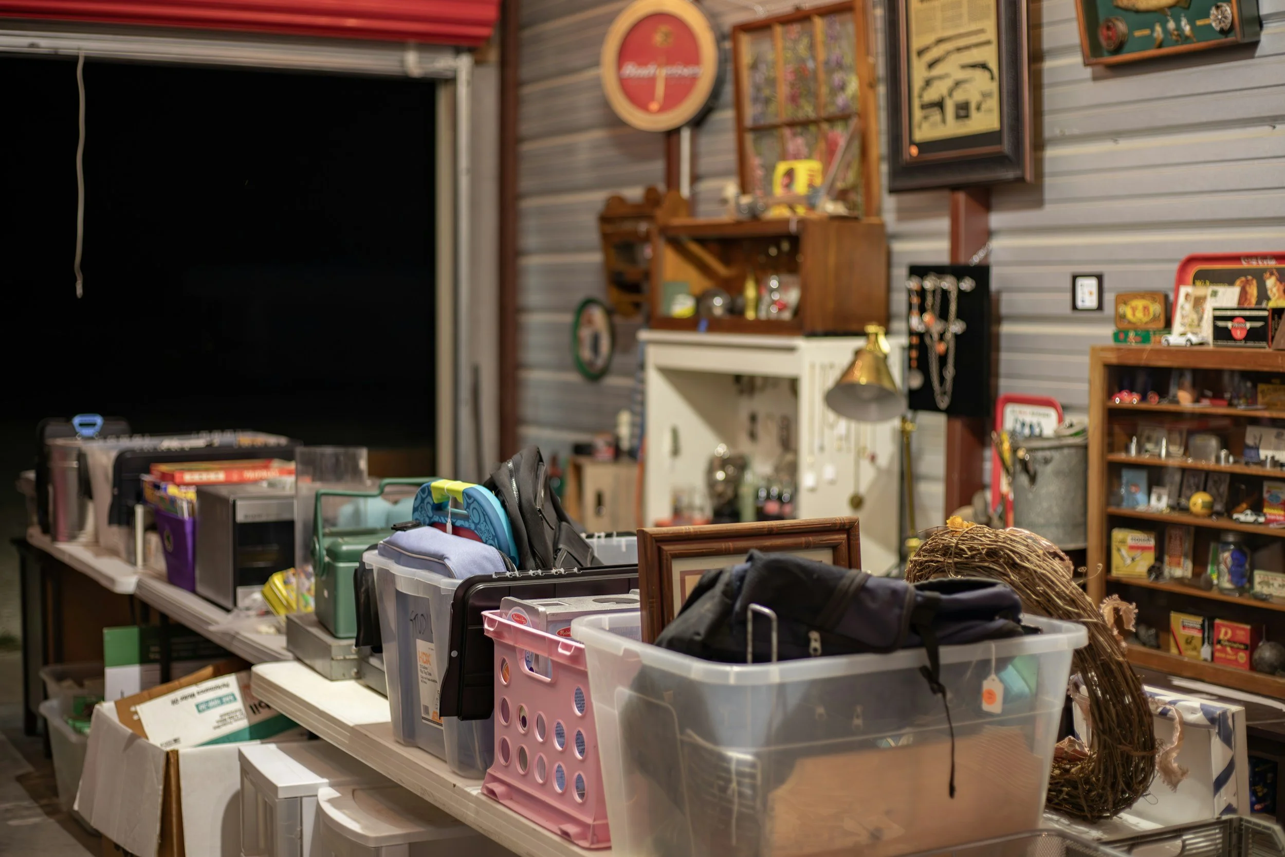 Tables with various items such as shoes, storage bins, books, and decorative objects inside a room with gray paneled walls.
