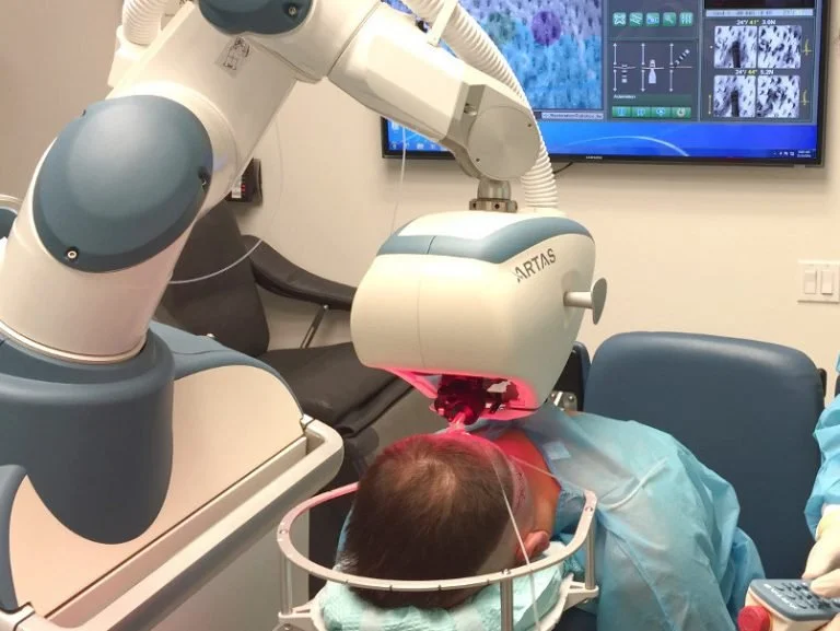 Doctor performing an ARTAS hair transplant surgery on a patient in a medical facility.