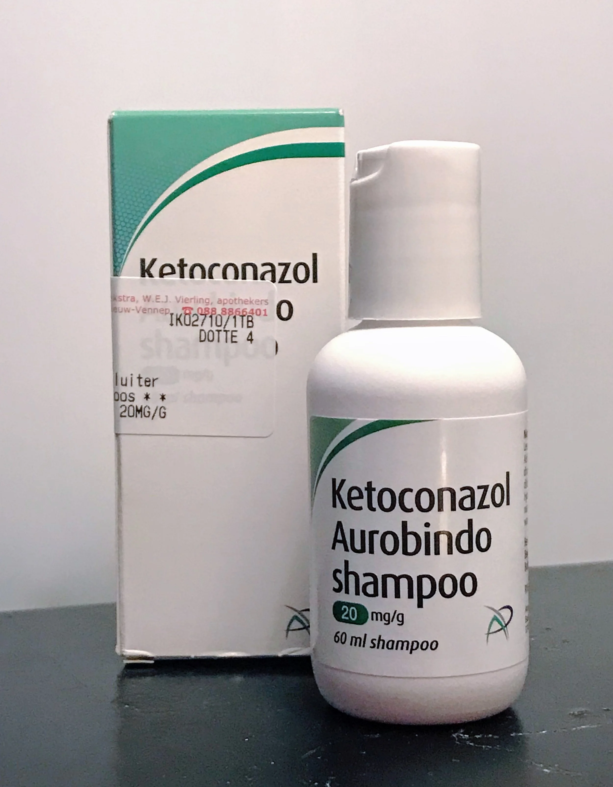 A box and a bottle of ketoconazole shampoo for dandruff treatment placed on a dark surface.