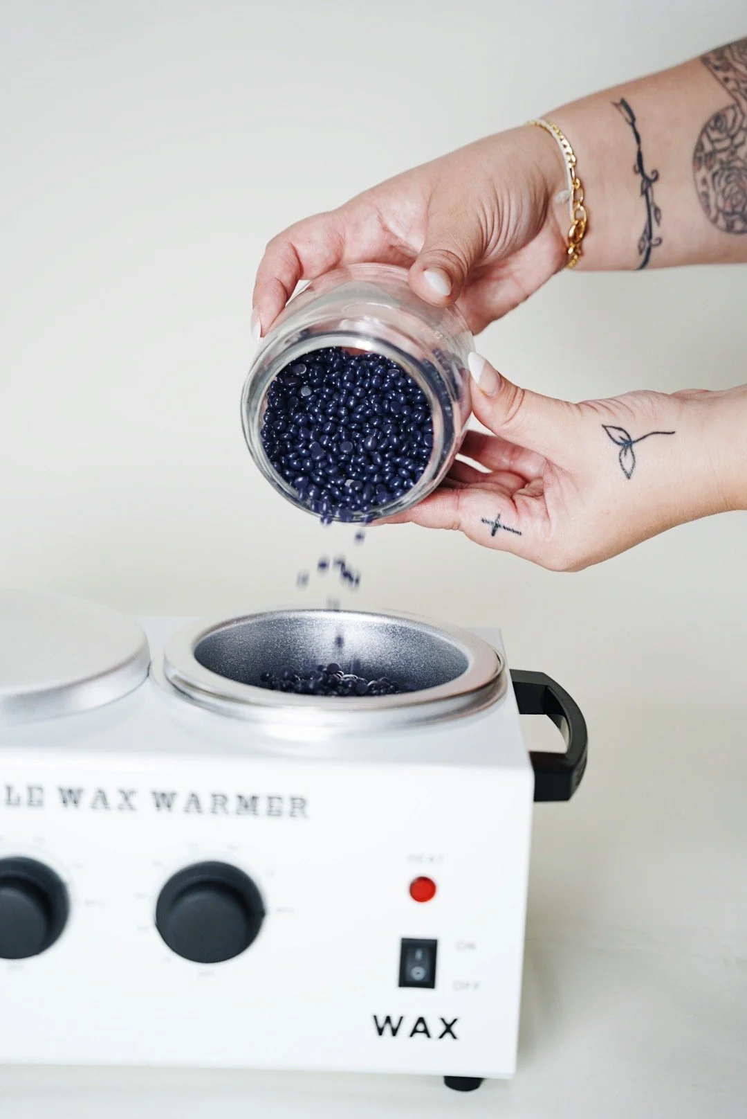Person pouring small dark beads into a wax warmer machine.