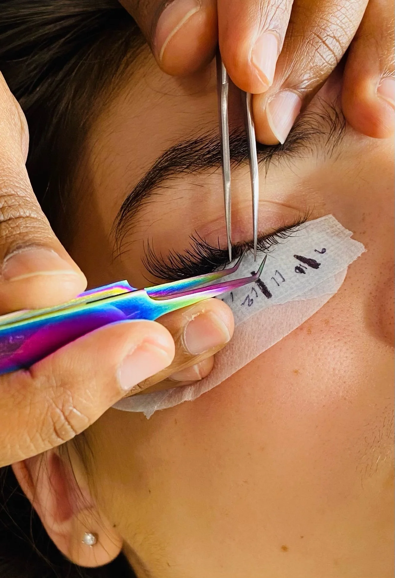 Close-up photo of a person receiving a eyelash service , with a technician using tweezers to apply lash extensions.
