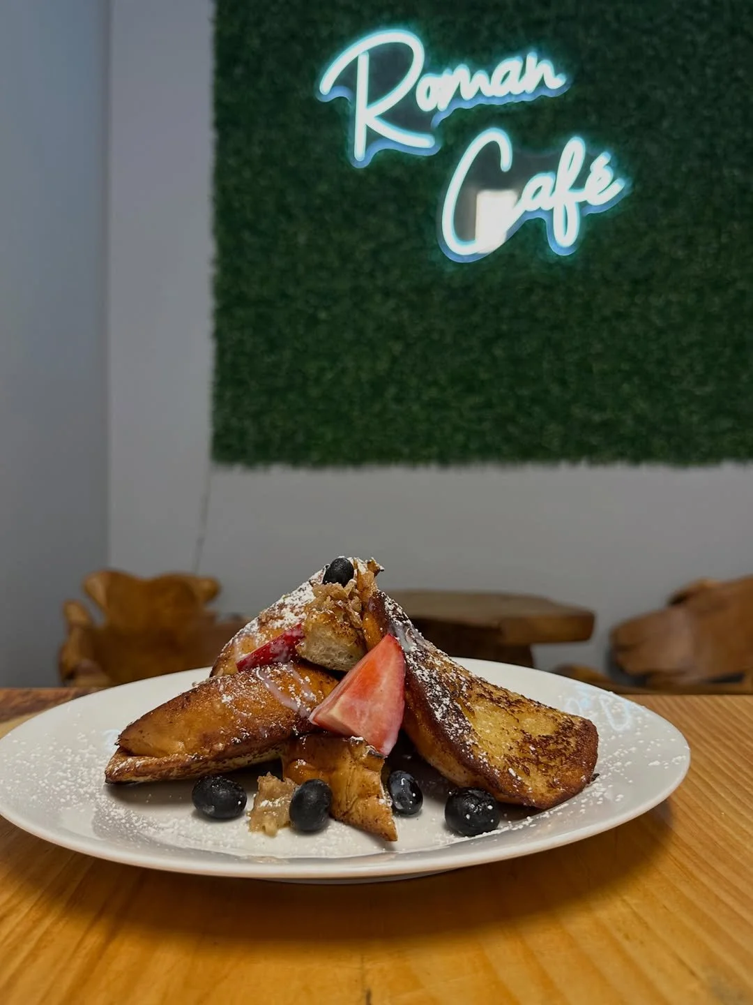 Plate of French toast with strawberries, blueberries, and powdered sugar, set on a wooden table at Romah Café.