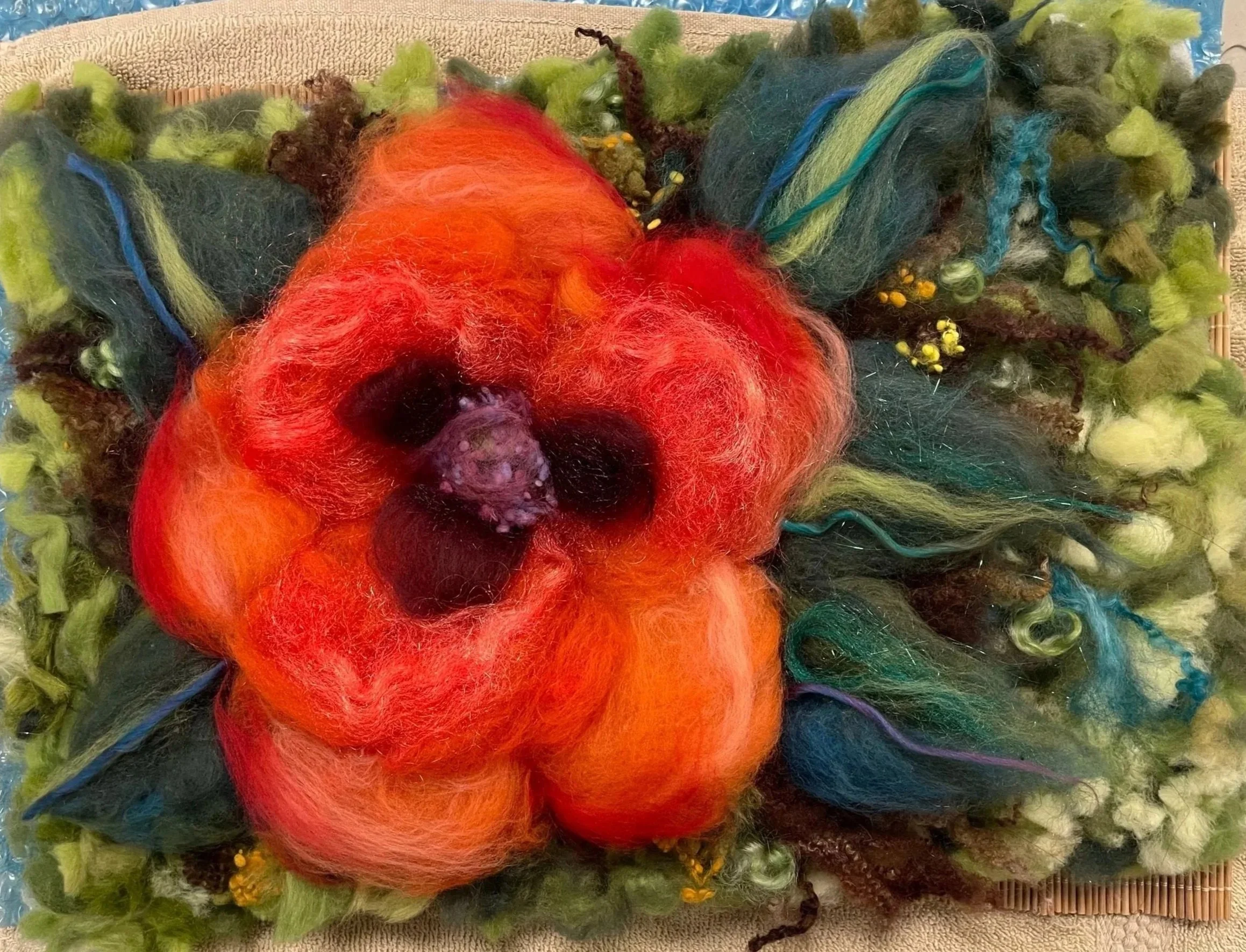 Close-up of a tangled mix of multicolored wool fibers, primarily red, green, blue, and black, on a textured beige surface.