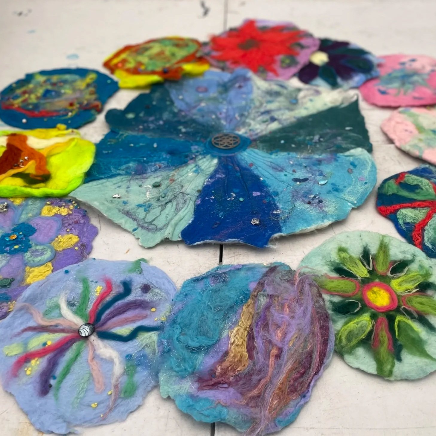 Colorful, handmade felted wool butterfly and flower crafts with vibrant colors and glitter details, laid out on a white surface.
