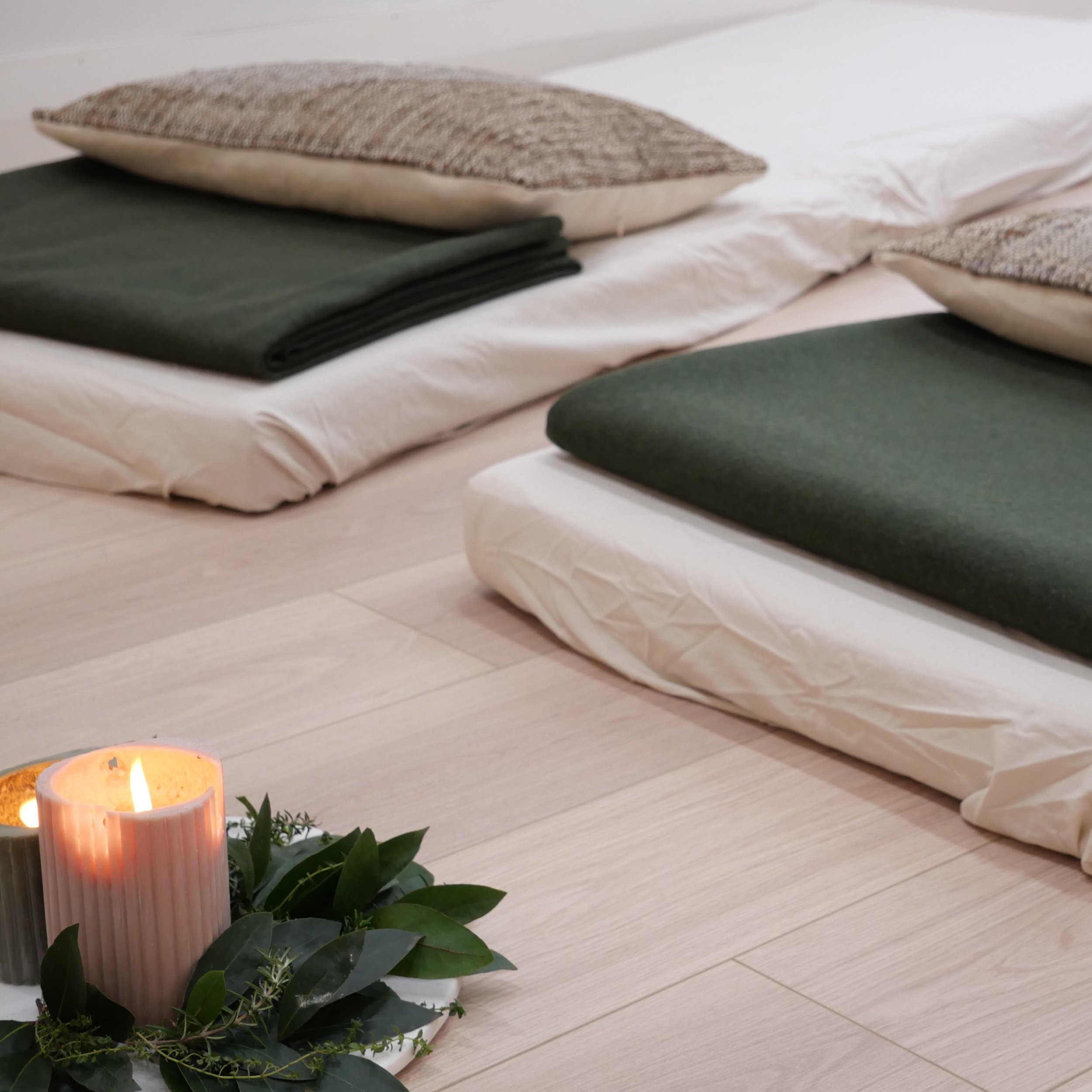 Decorative candle holder with lit candle and green plants next to a yoga mat, on a wooden floor.