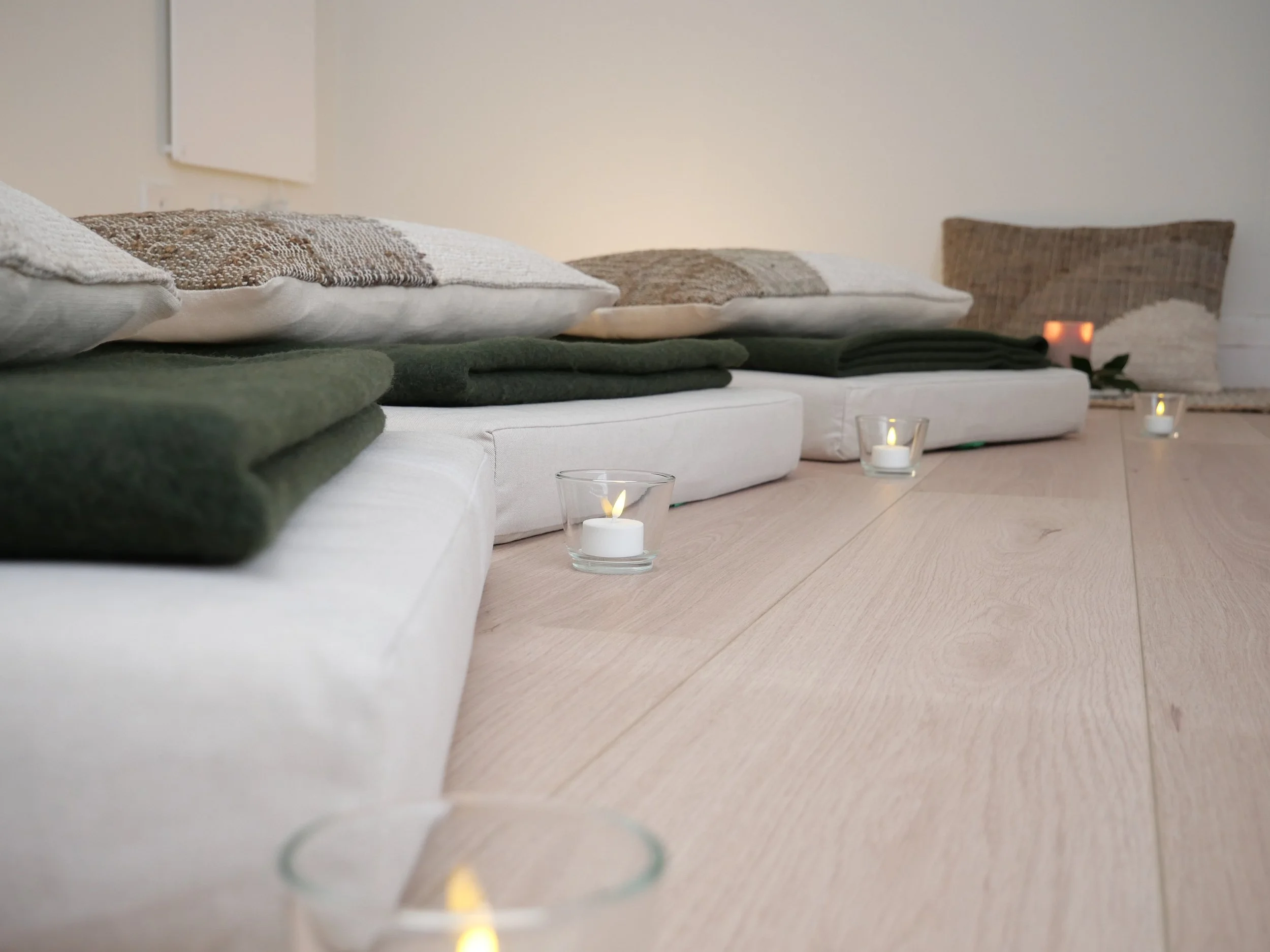 A row of pillows with various textures and patterns on a white sofa, illuminated with candles on the floor in front.