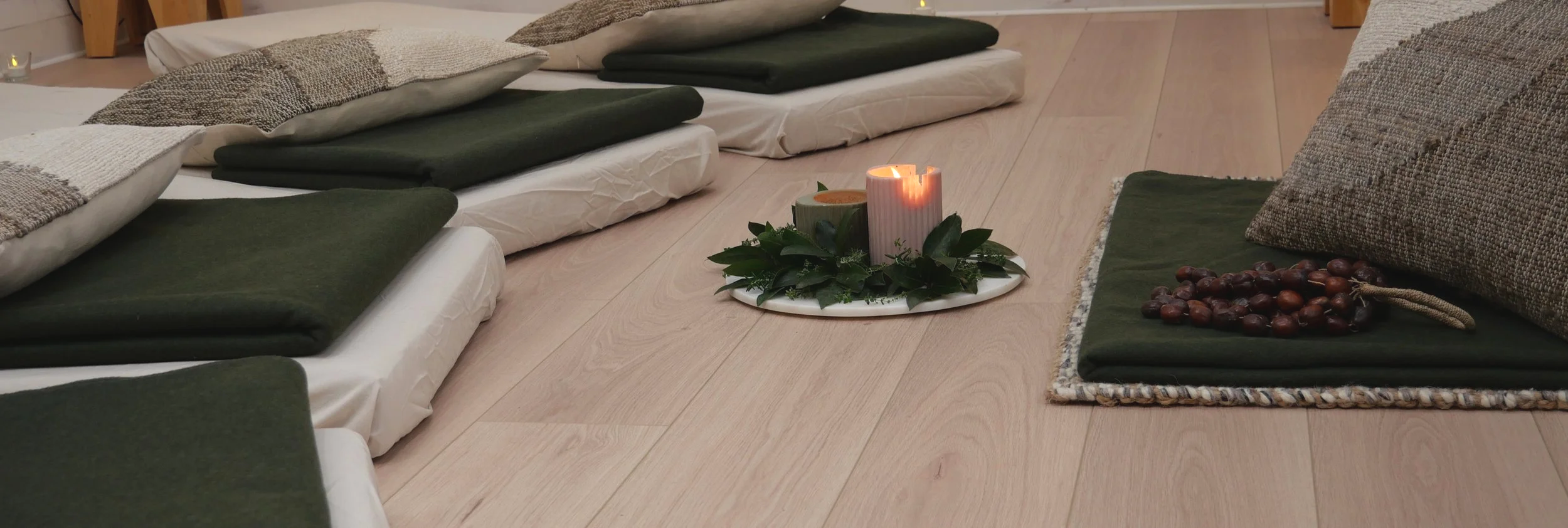 A cozy floor seating area with cushions, blankets, a lit candle, and a plate of chestnuts arranged for a calm, inviting atmosphere.