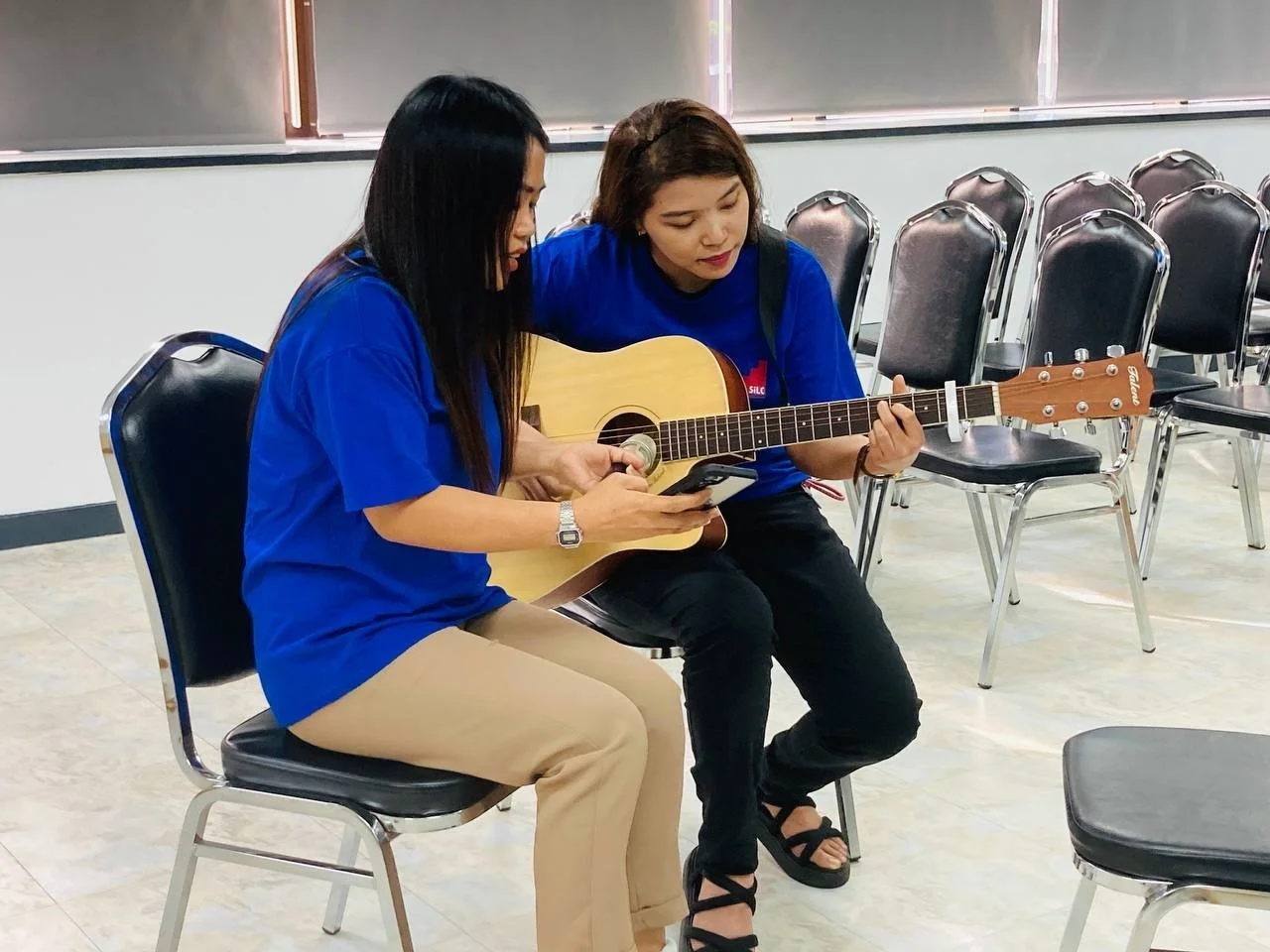 Two young women practicing live music and holding a guitar.